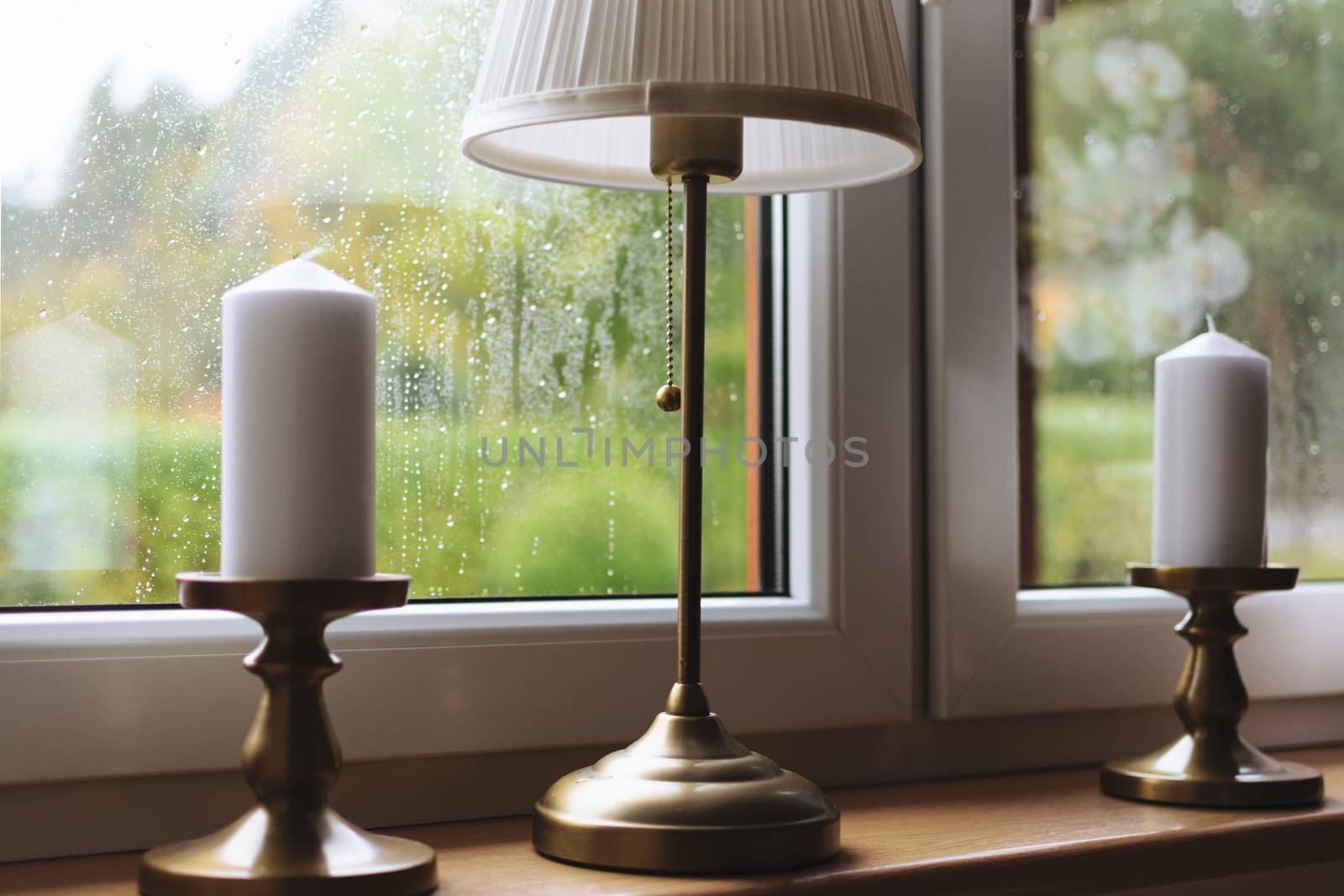 Nostalgic background concept - rain drops on a window with candles and a light at home during autumn rainy weather