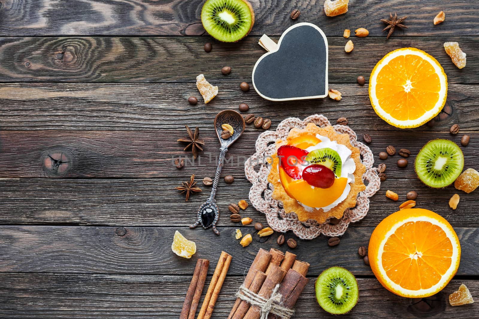 Rustic wooden background with fruit tart, spices, kiwi and oranges. Heart chalkboard for text.Top view, flat lay.
