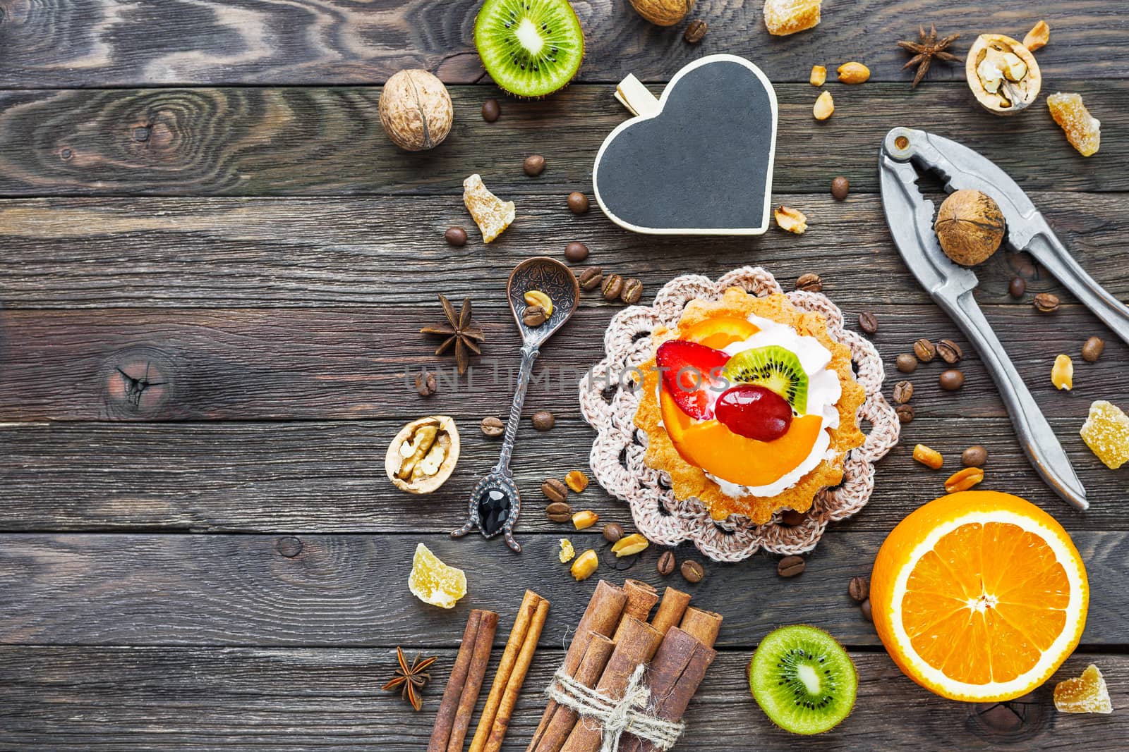 Rustic wooden background with fruit tart, spices, kiwi and oranges. Heart chalkboard for text.Top view, flat lay.