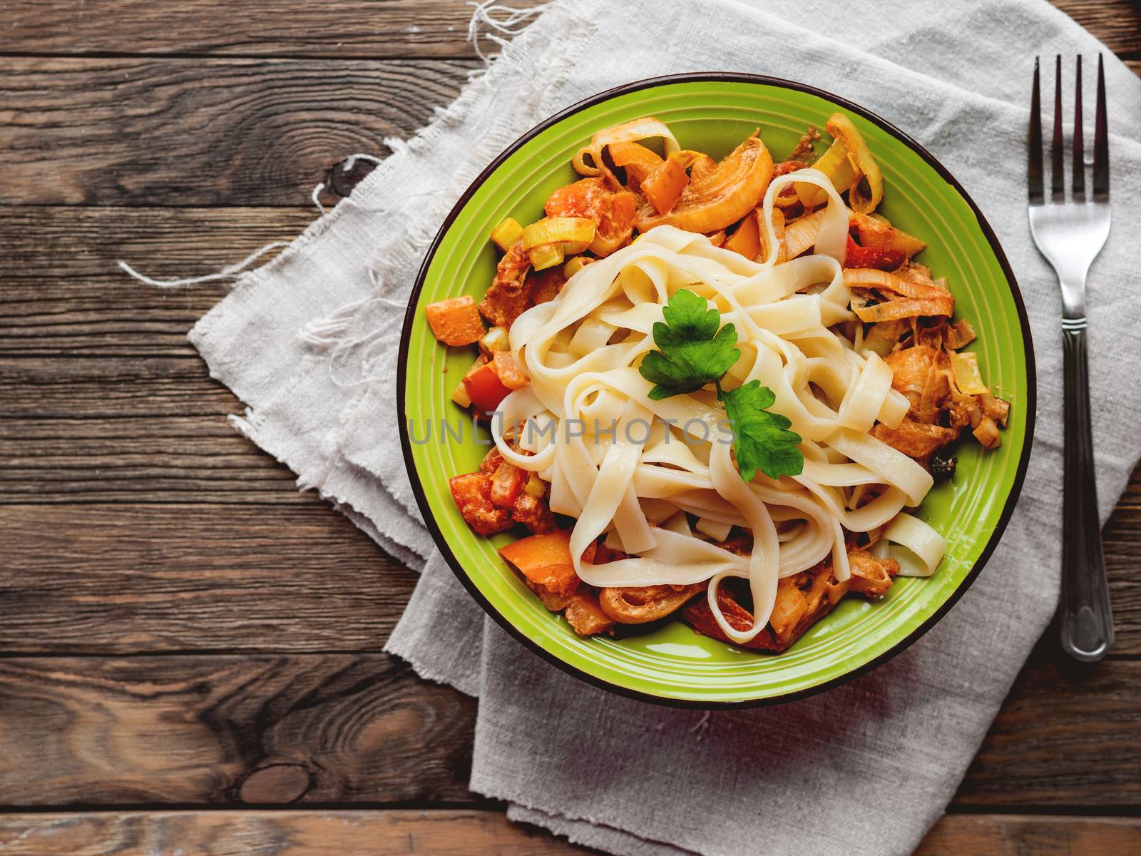 Green plate with tasty fettuccine and tomato sauce. Top view on wooden table, napkin and bowl with pasta. Italian cuisine.