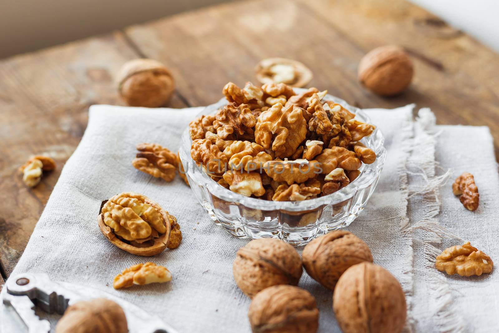 Glass bowl with walnuts on rustic homespun napkin. Healthy snack on old wooden background.