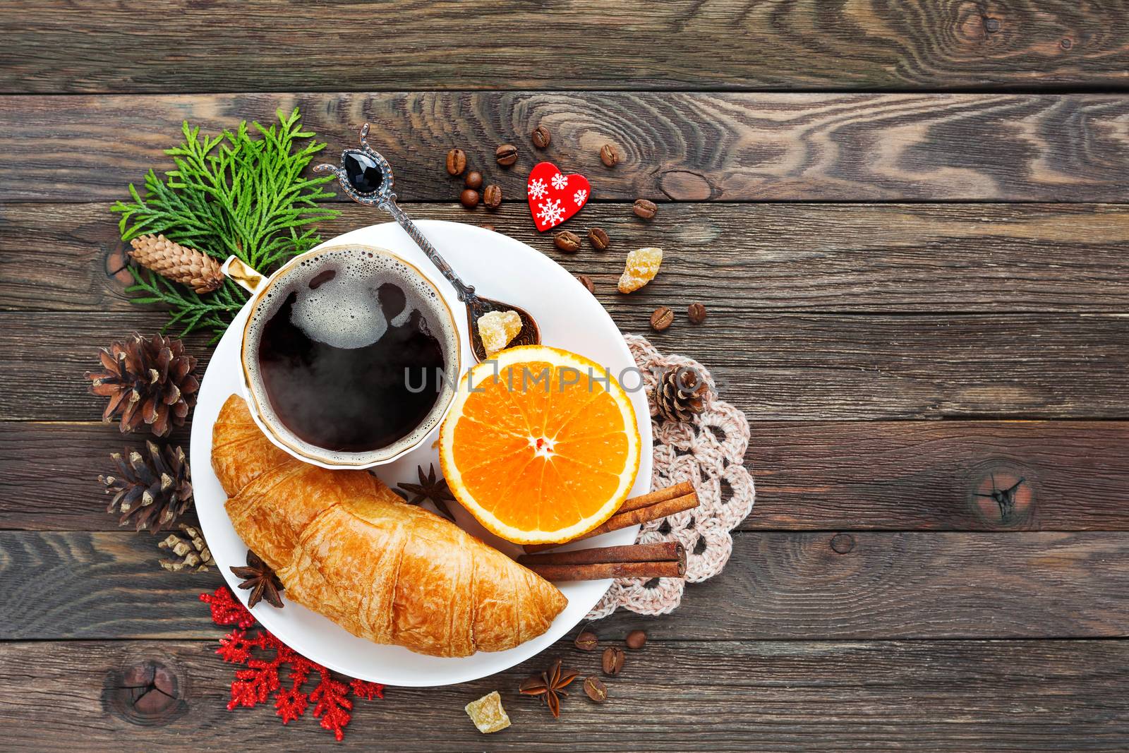 Christmas and New Year background with continental breakfast - cup of hot coffee with cinnamon, fresh orange and croissant. Decorations - snowflake, crochet napkin, pine cones.