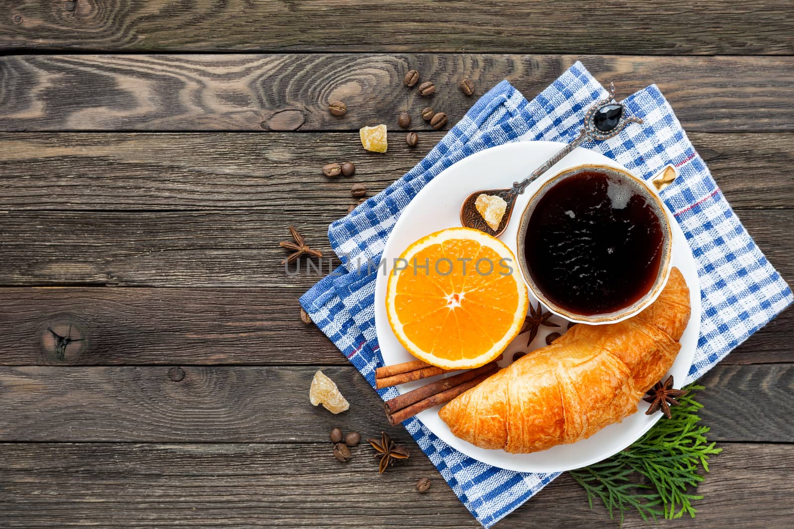 Continental breakfast - cup of hot coffee, croissant and orange. Tasty food on plaid blue napkin. Rustic wooden background. Top view, place for text.