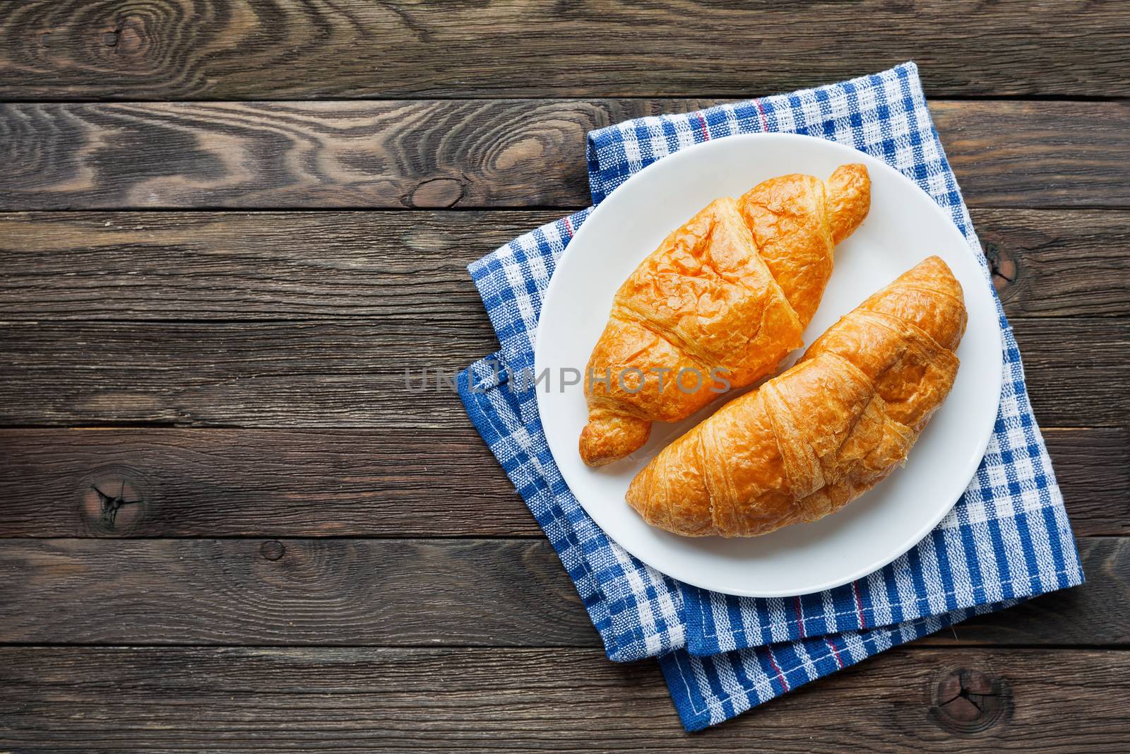 Continental breakfast background - pair of croissants on plaid blue napkin. Rustic wooden background with place for text. Top view.