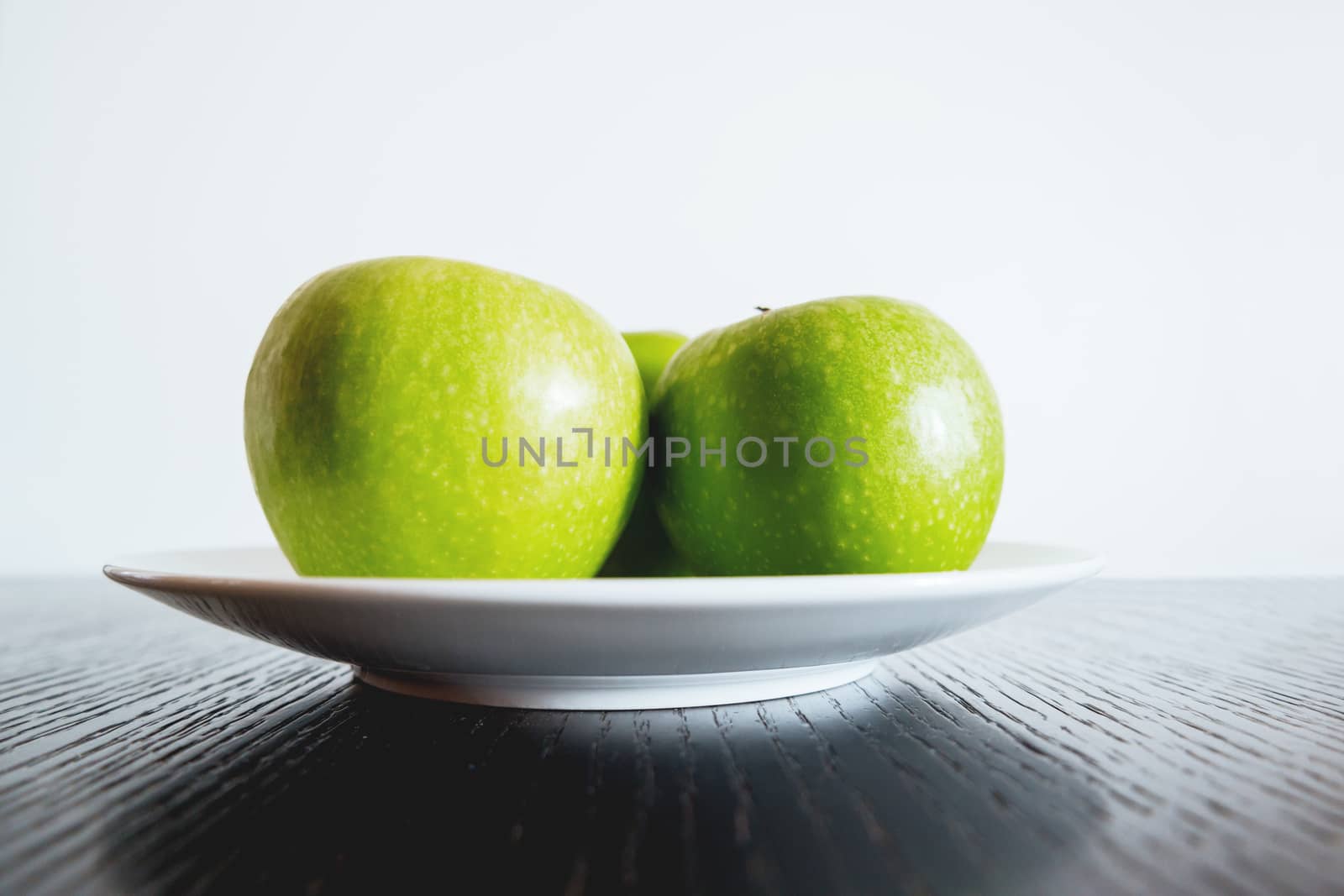 Three fresh green apples on white plate.