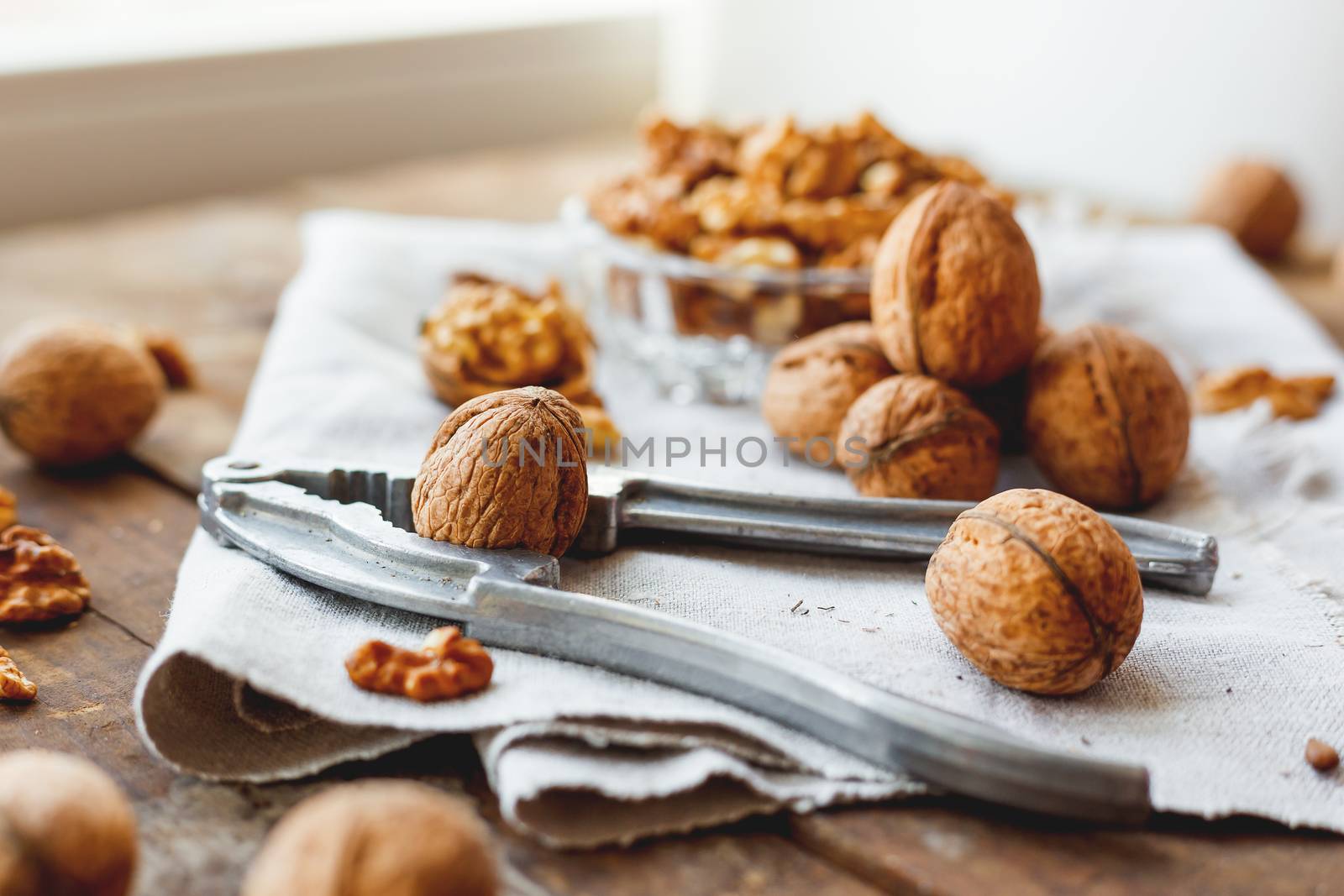 Glass bowl with walnuts on rustic homespun napkin. Healthy snack on old wooden background.
