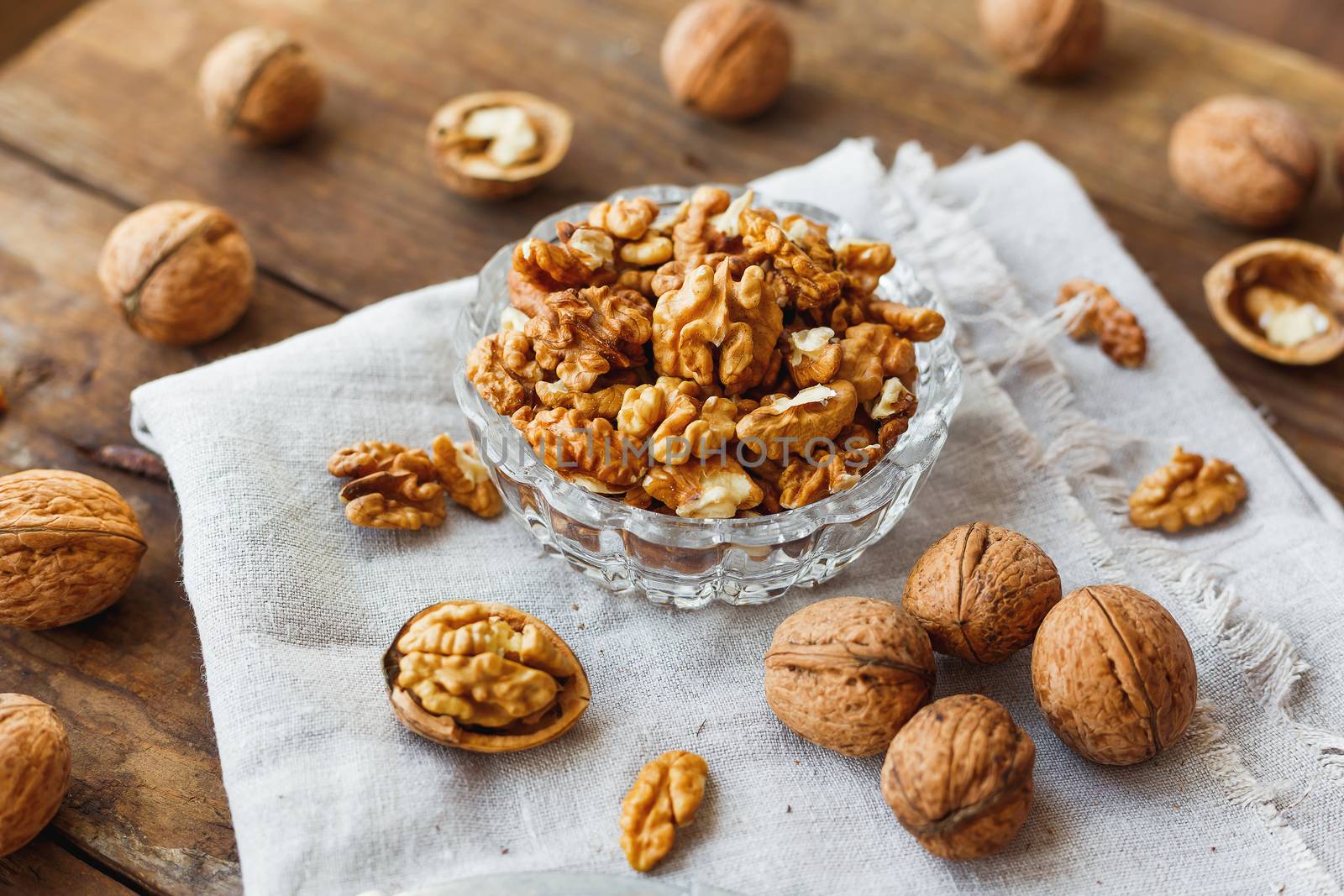 Glass bowl with walnuts on rustic homespun napkin. Healthy snack on old wooden background.