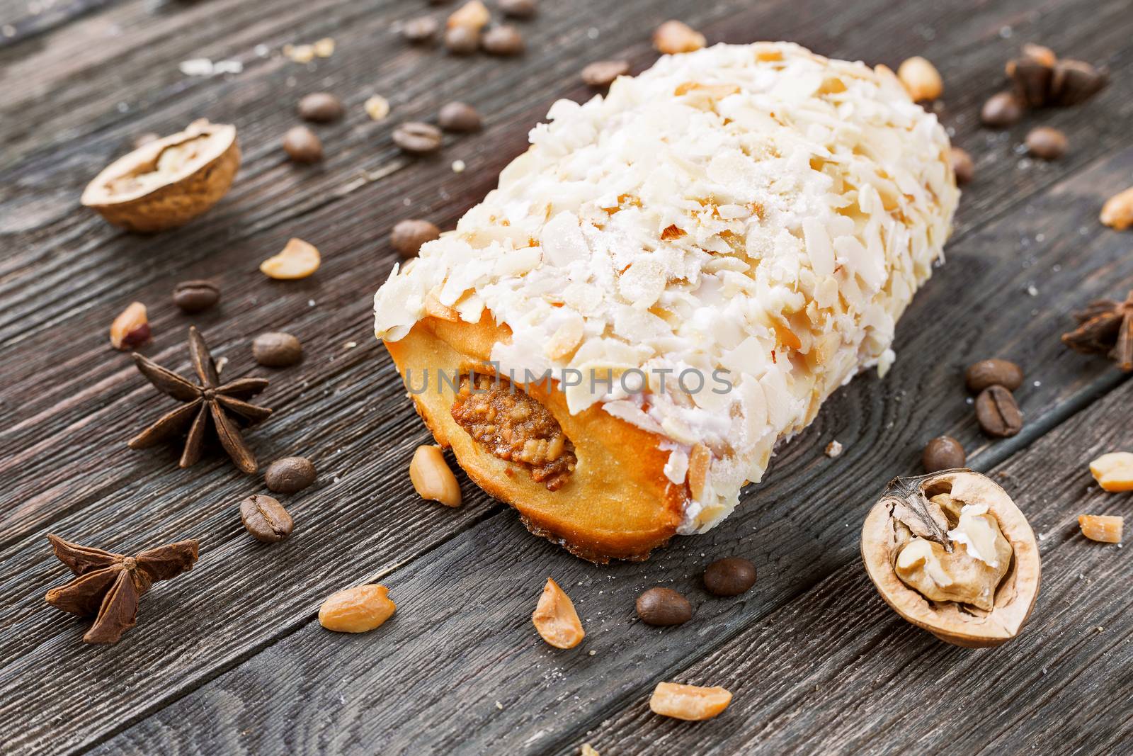 Bun with marzipan on rustic wooden background. Different spices around peanut dessert - anise stars, coffee beans, walnuts.