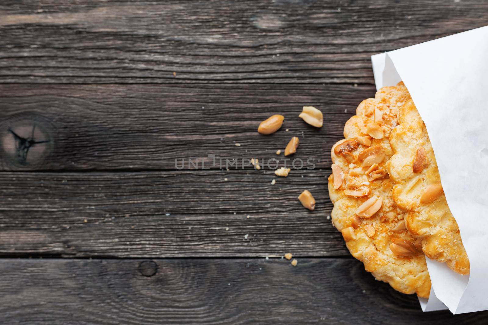Tasty tart with peanuts in white paper bag. Rustic wooden background with sweet dessert. Top view.