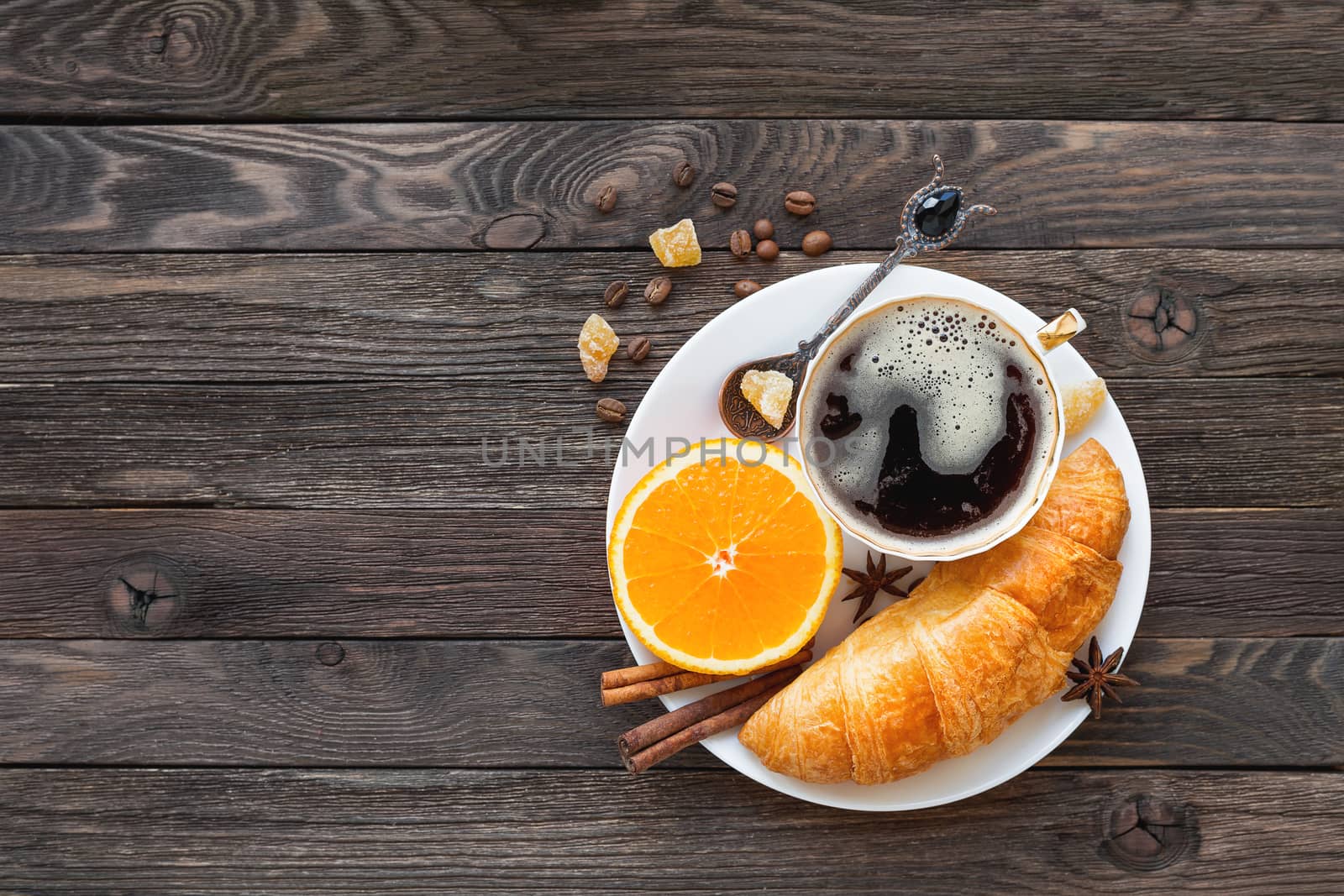 Continental breakfast - cup of hot coffee, croissant and orange. Tasty food on rustic wooden background. Top view, place for text.