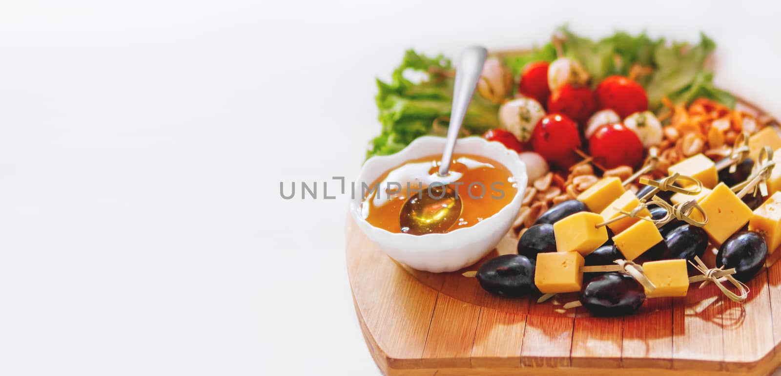 Wooden cutting board with snacks - honey, olives with cheese, vegetables. White copy space.