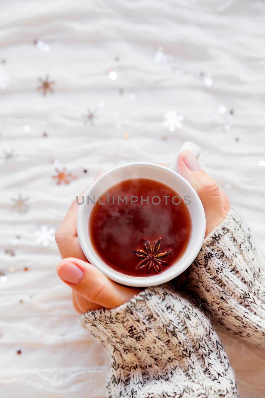 Woman holds a cup of hot tea with anise star. Winter fabric background with sparkling silver snowflakes.