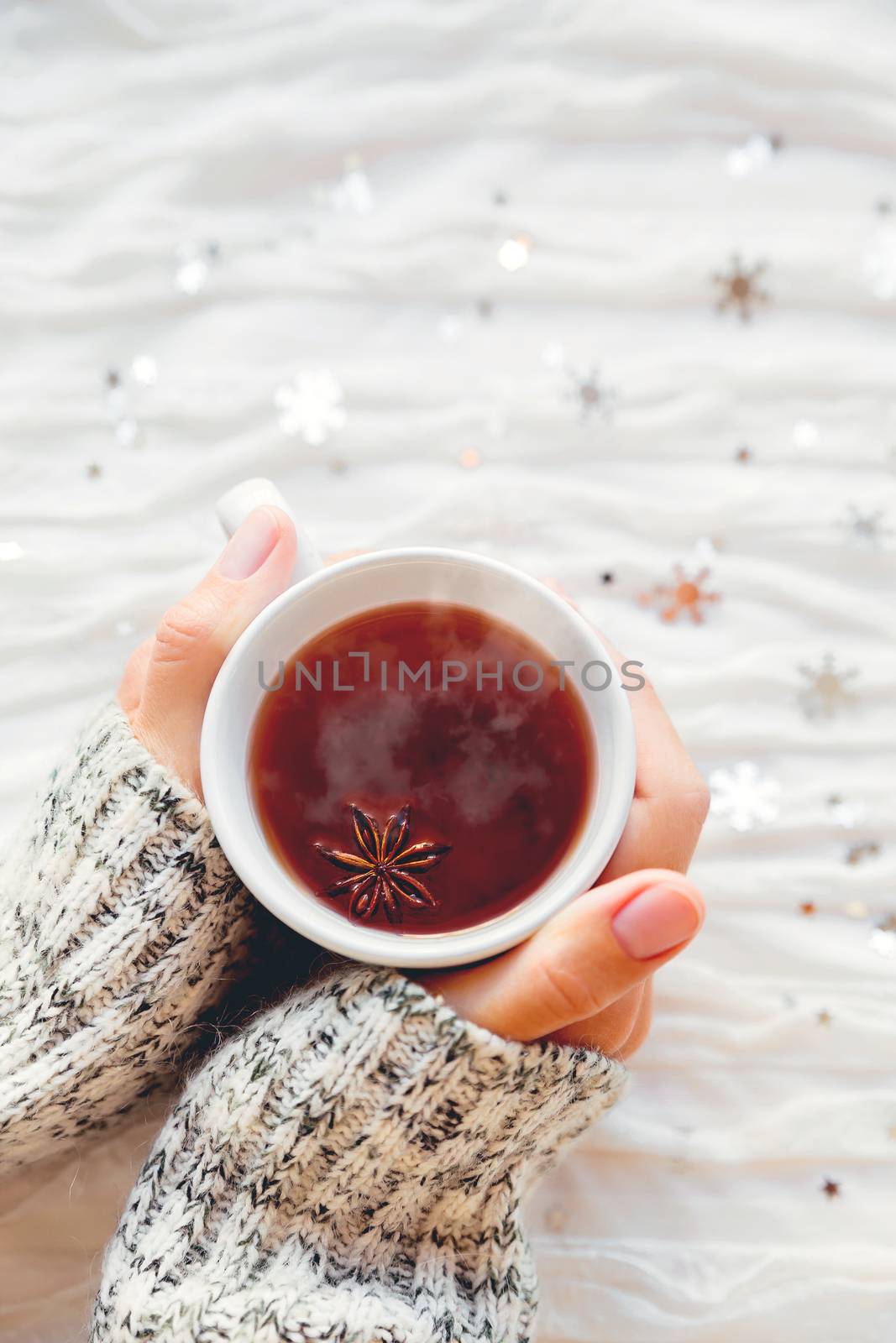 Woman holds a cup of hot tea with anise star. Winter fabric background with sparkling silver snowflakes.