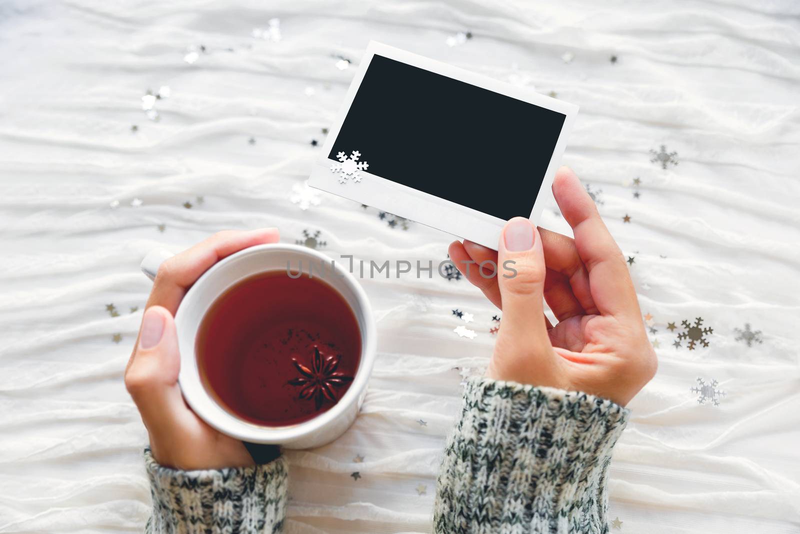 Woman holds a cup of tea and photo. Winter fabric background with sparkling silver snowflakes. Empty photo frame for your text or picture.