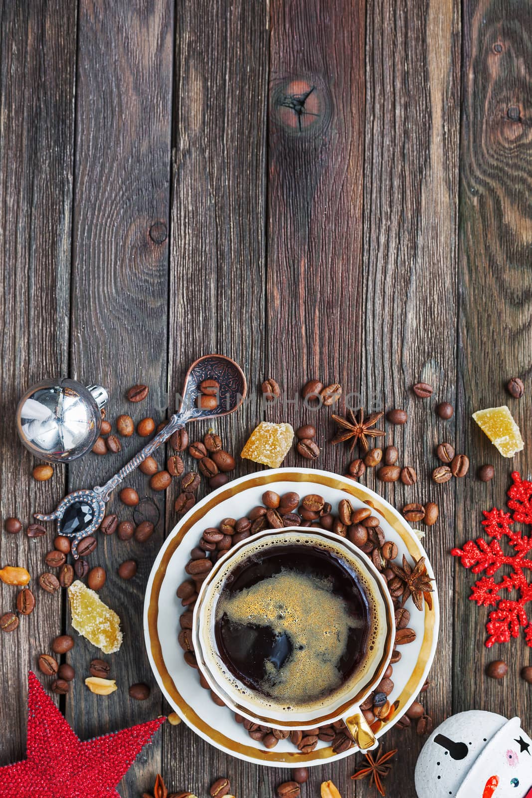 Rustic wooden background with cup of coffee and New Year decorations. White vintage dinnerware and spoon. Christmas beverage with ginger and anise. Top view, place for text.