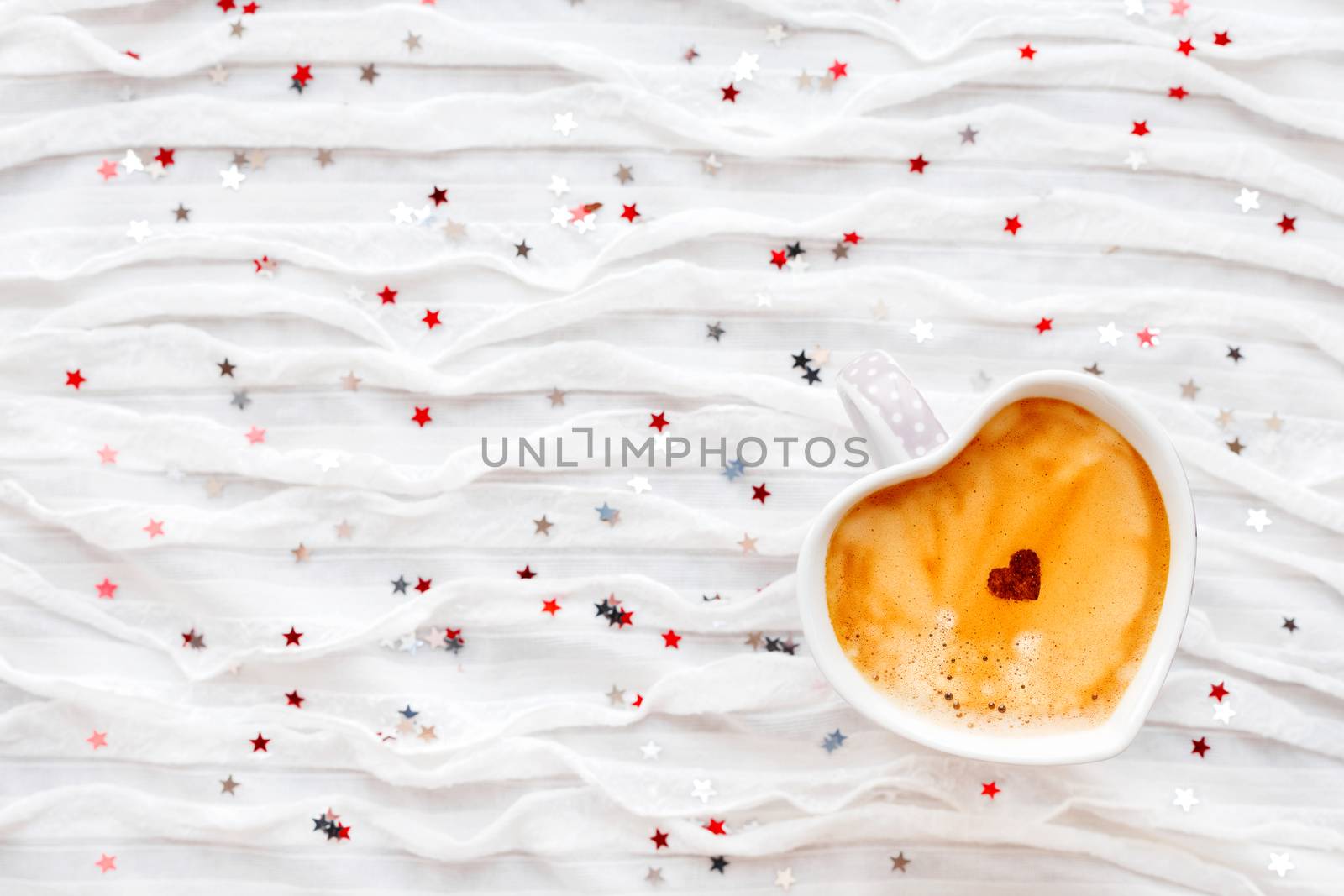Cup of hot coffee with cinnamon heart. Winter and Valentine's Day fabric background with sparkling silver and red confetti.