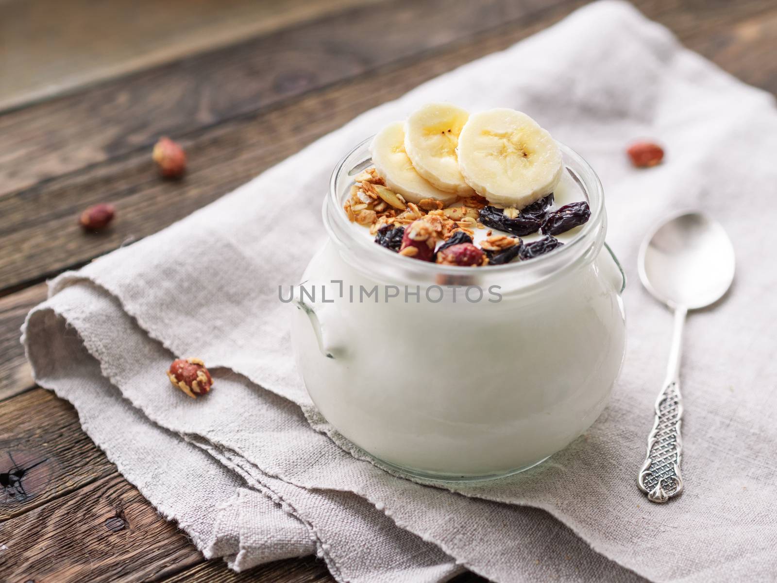Natural homemade yogurt in a glass jar. Healthy food for breakfast with muesli. Jar with granola and banana sliceson linen tablecloth on on wooden table.