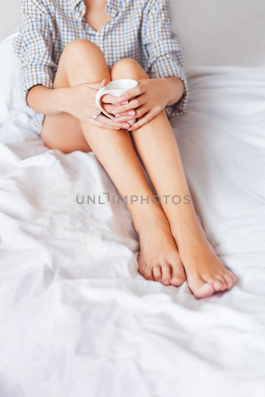 Woman in shirt sitting in bed with a cup of hot coffee. Cozy morning at home. Place for text.