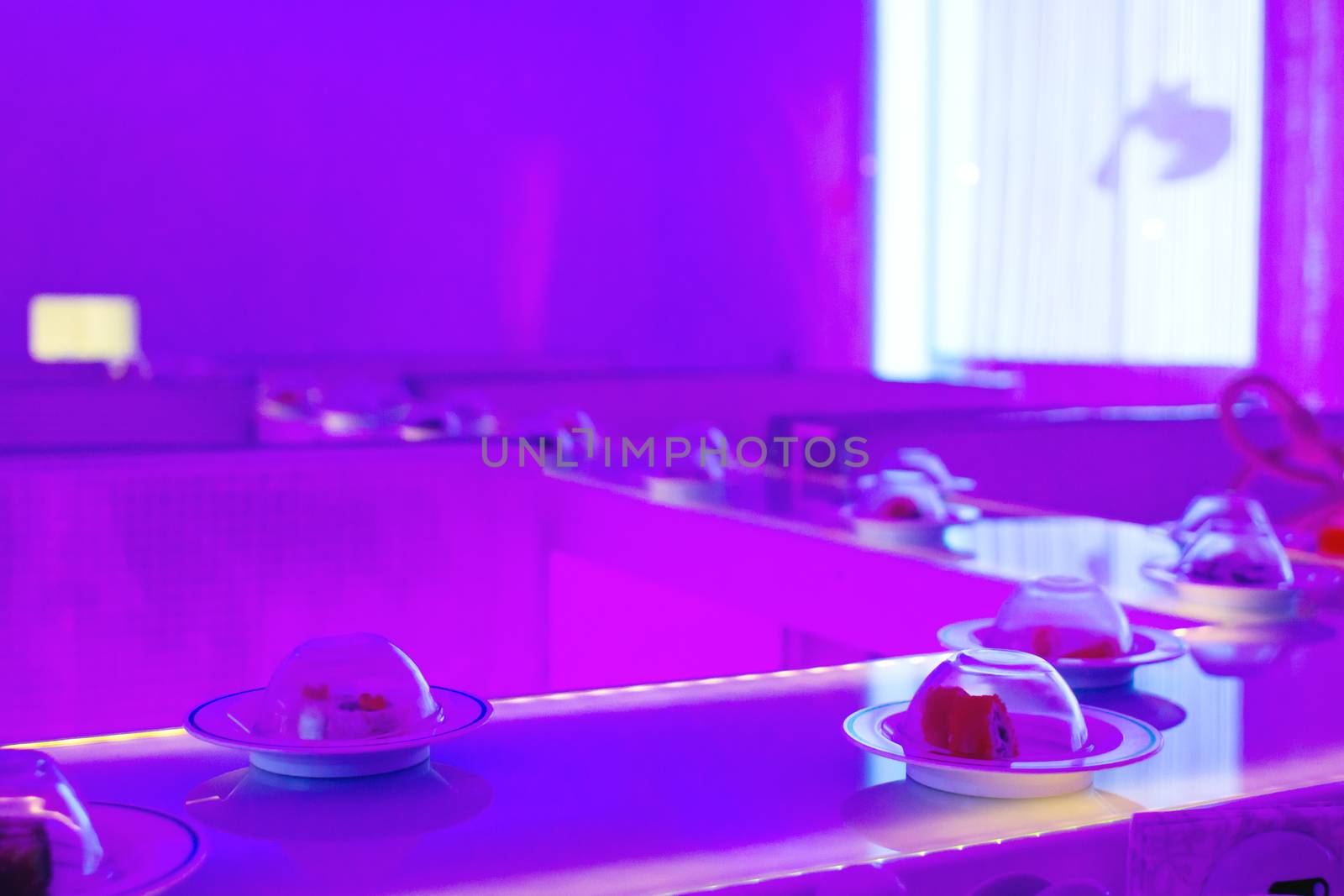 Conveyor serving dishes. Neon-purple lights over the plates with the sushi rolls.