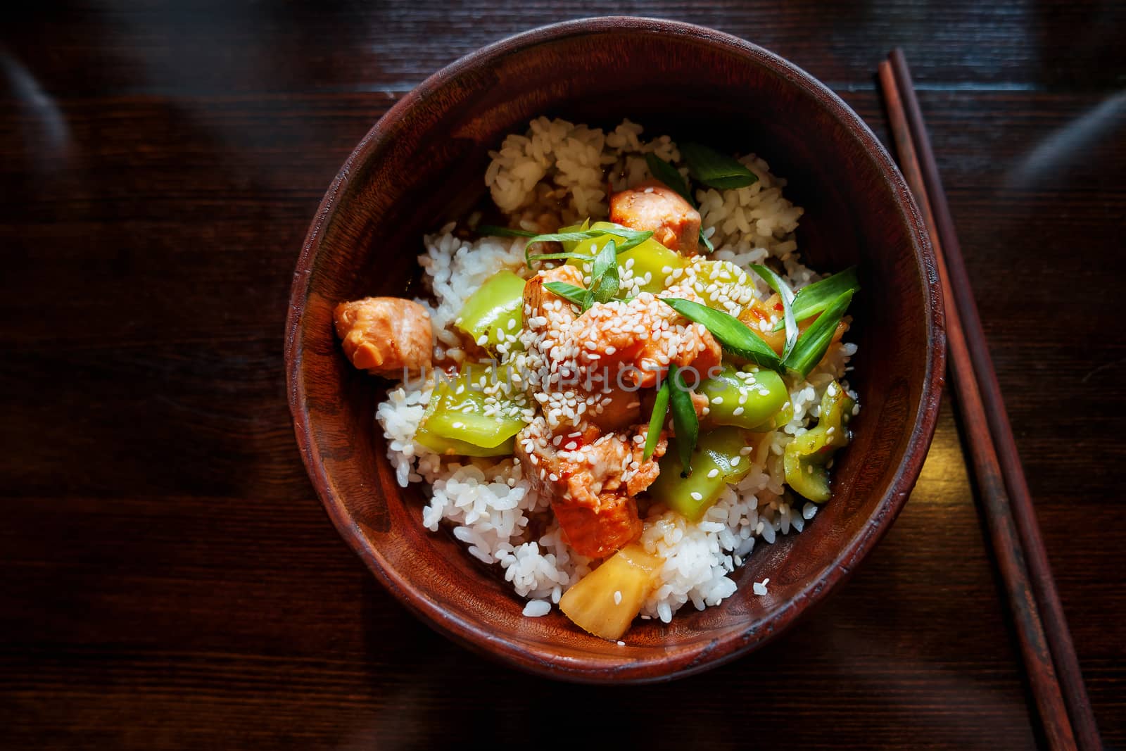 Asian cuisine - rice in sauce with stir fried vegetables, pineapple and salmon. Wooden bowl with chopsticks.