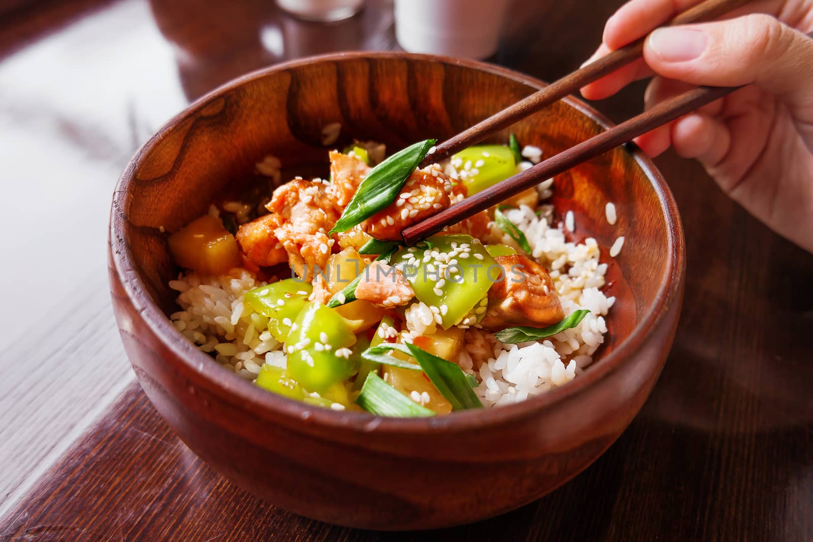 Asian cuisine - rice in sauce with stir fried vegetables, pineapple and salmon. Wooden bowl with chopsticks.