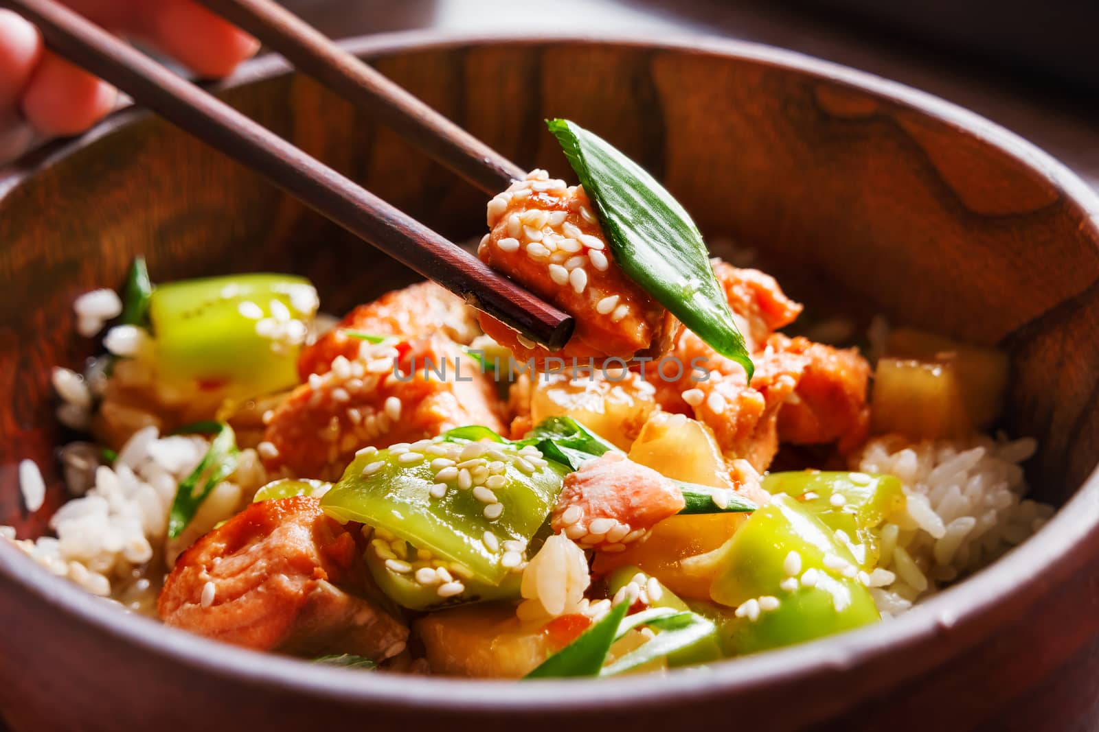 Asian cuisine - rice in sauce with stir fried vegetables, pineapple and salmon. Wooden bowl with chopsticks. Close up.