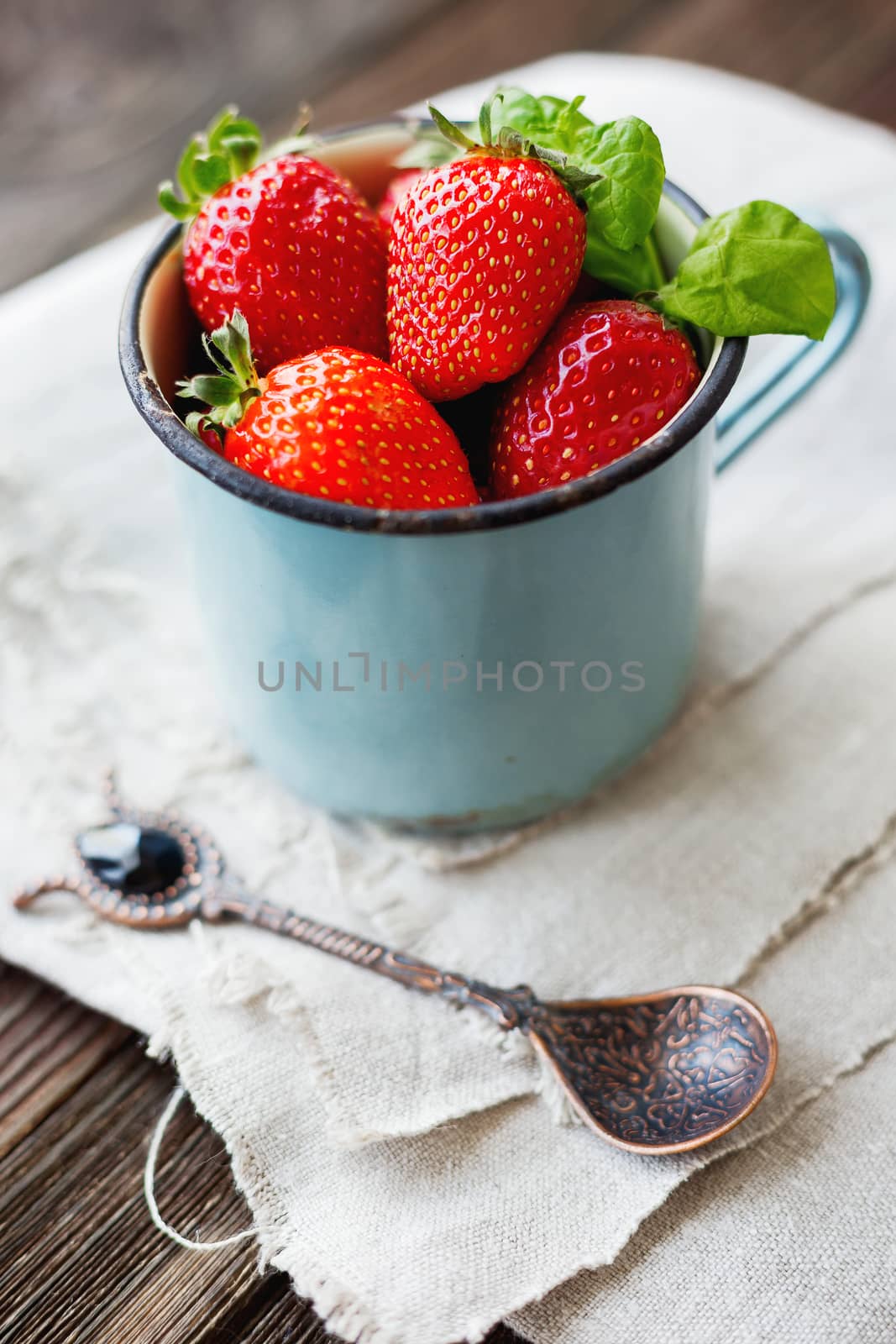 Fresh juicy strawberries in old rusty mug. Rustic wooden background with homespun napkin and vintage spoon.