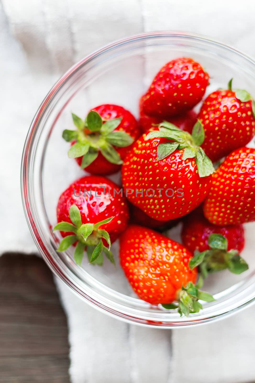 Fresh juicy strawberries in glass bowl. Rustic background with homespun napkin. Top view.