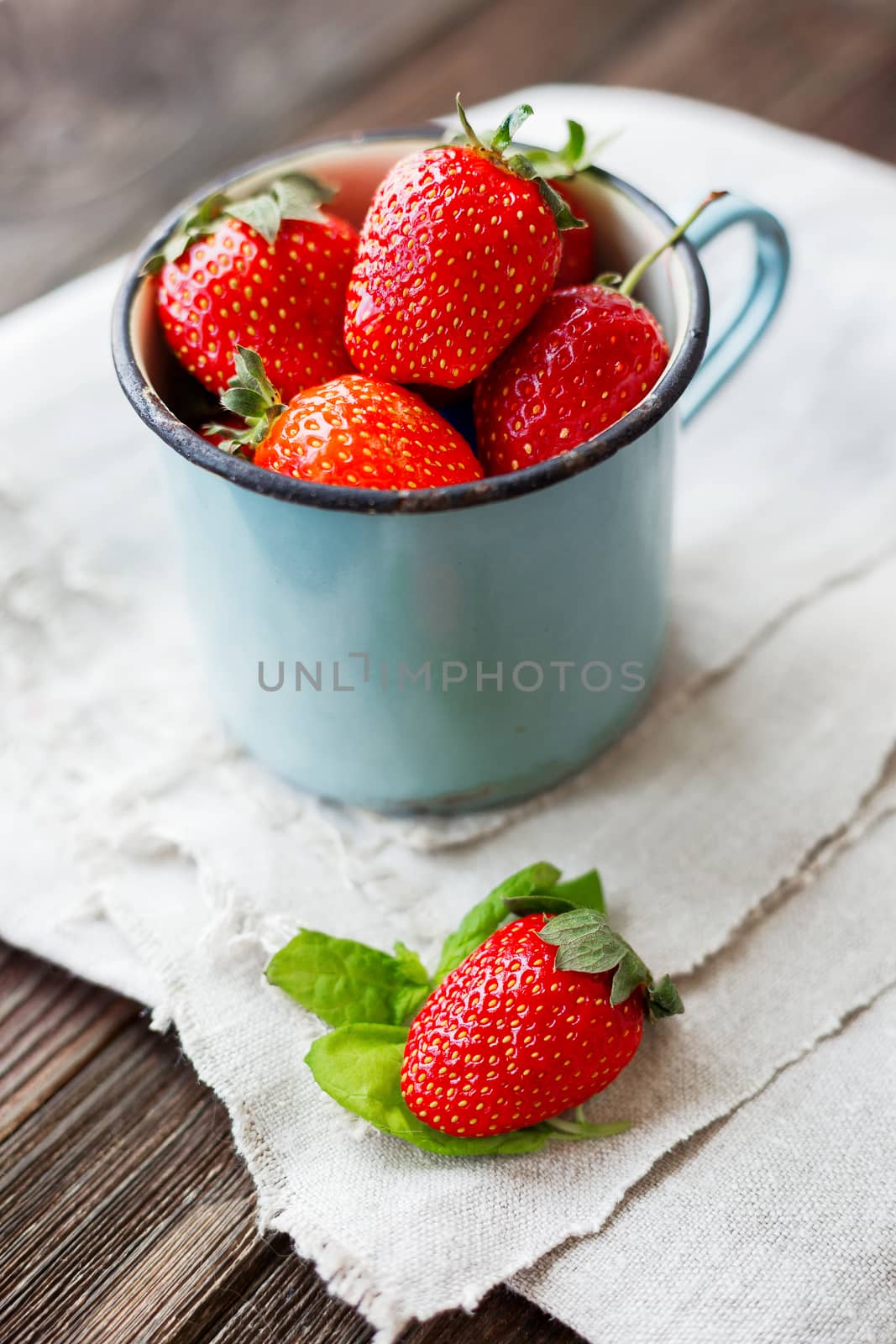 Fresh juicy strawberries in old rusty mug. Rustic wooden background with homespun napkin.
