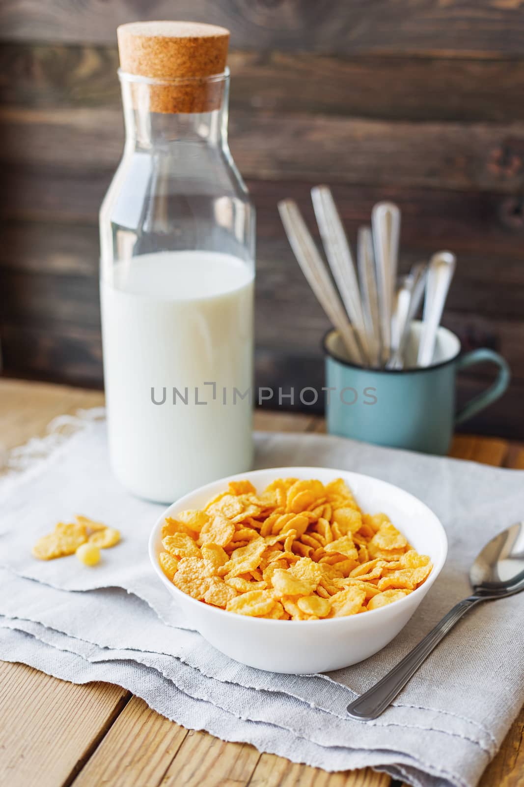 Tasty corn flakes in bowl with bottle of milk. Rustic wooden background with homespun napkin. Healthy crispy breakfast snack.