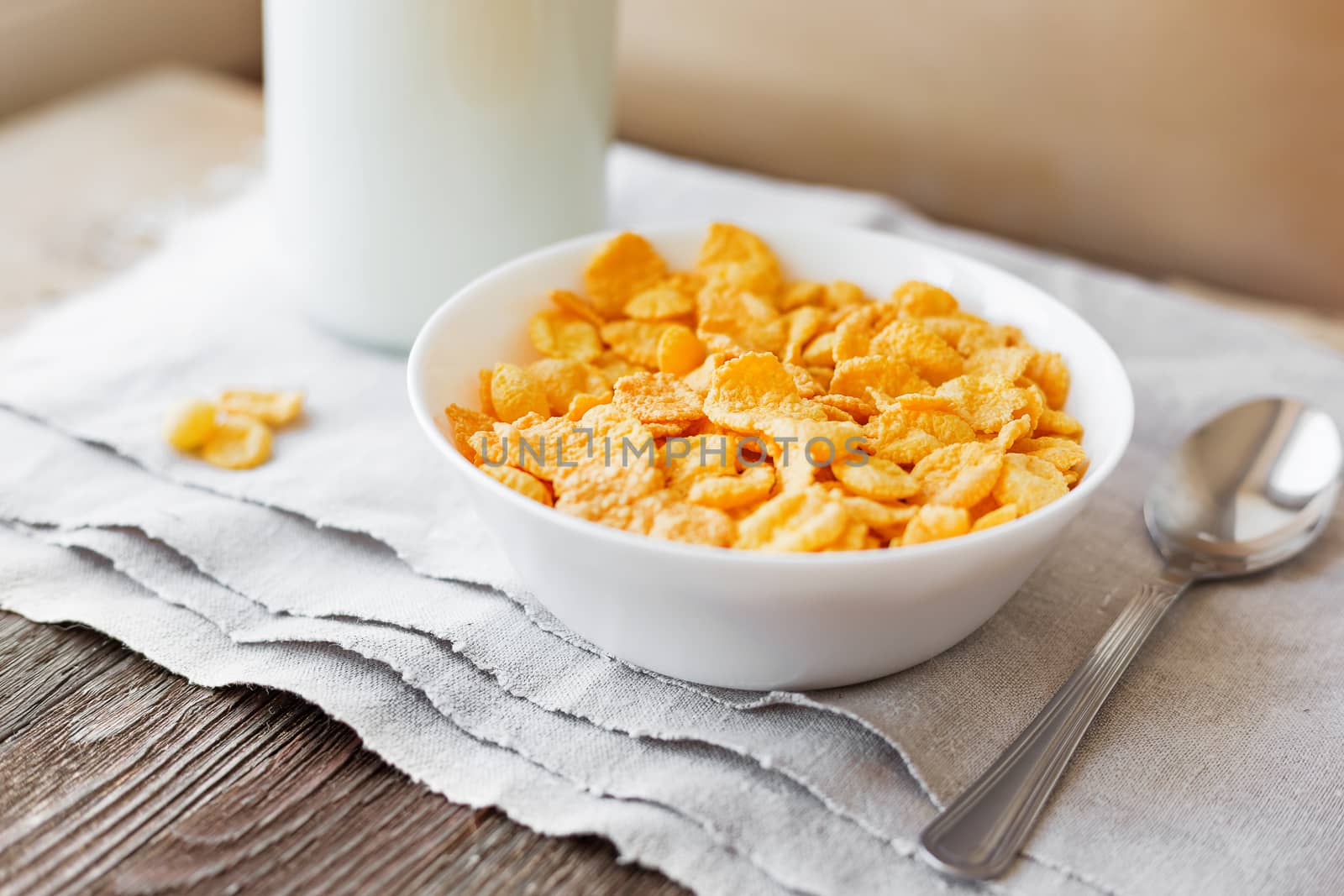 Tasty corn flakes in bowl with bottle of milk. Rustic wooden background with homespun napkin. Healthy crispy breakfast snack.
