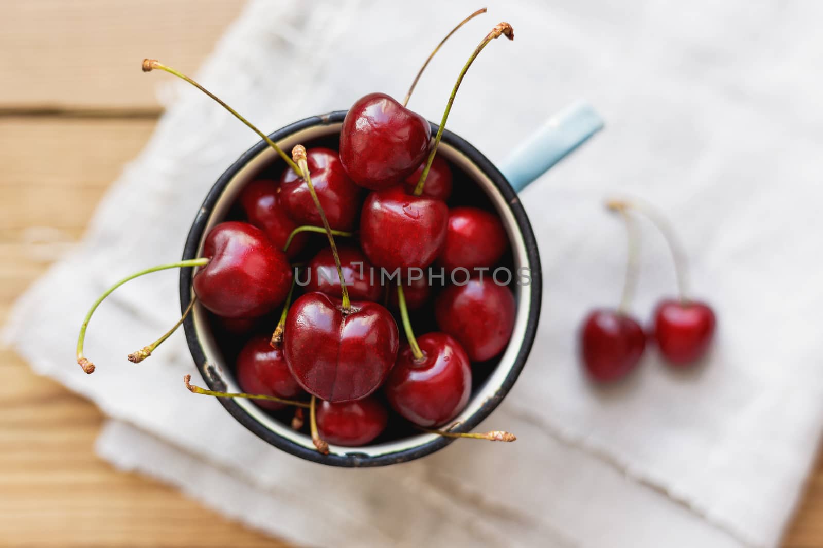 Fresh juicy sweet cherries in old rusty mug. Rustic background with homespun napkin.
