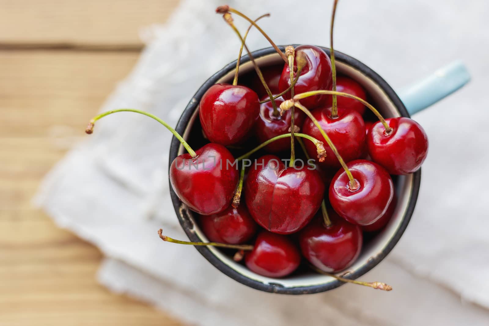 Fresh juicy sweet cherries in old rusty mug. Rustic background with homespun napkin.
