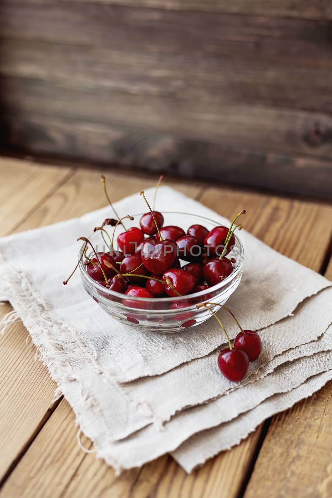 Fresh juicy sweet cherries in glass bowl. Rustic background with homespun napkin.