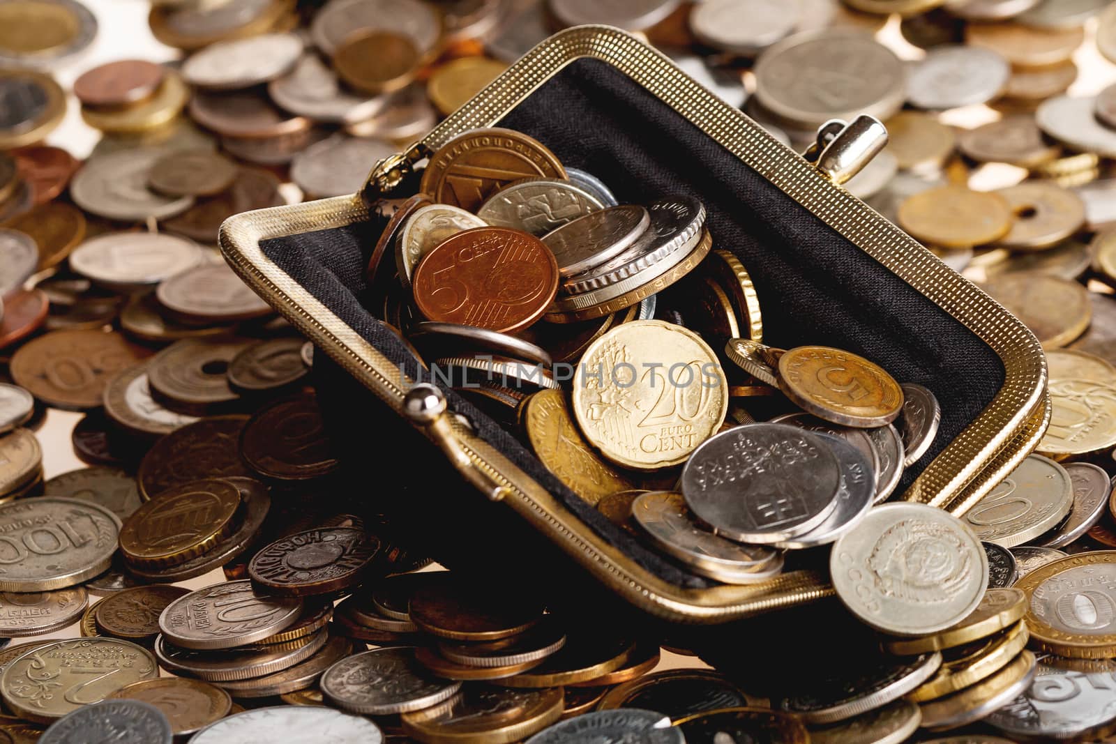 Black wallet with different coins. Big heap of shiny coins as background.