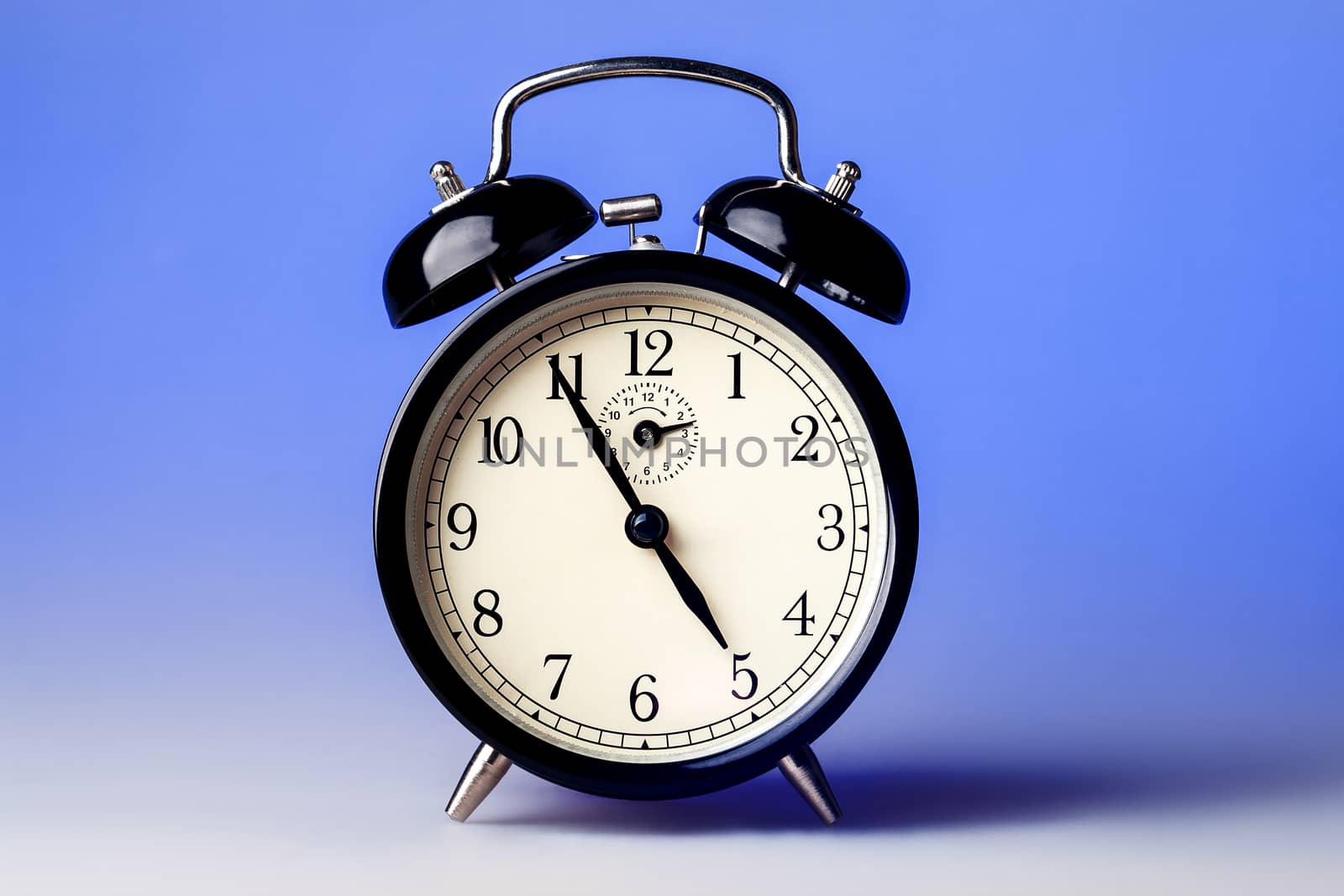 Black old fashioned alarm clock on blue background.