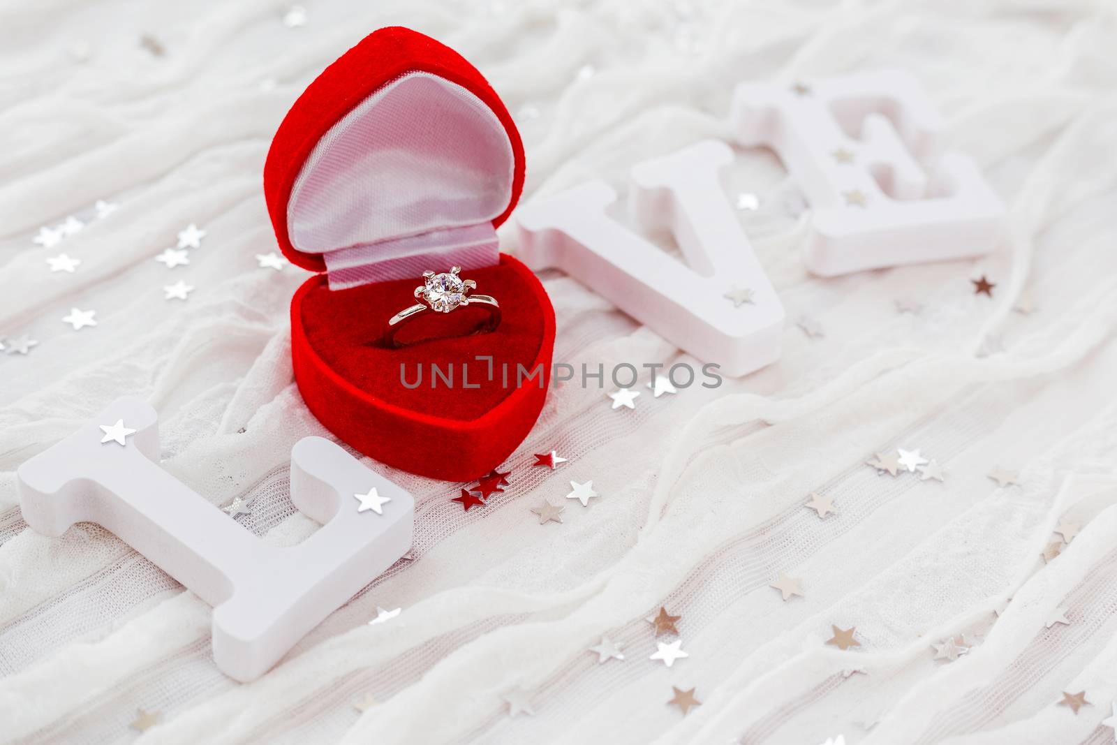 Word LOVE on white fabric background with engagement diamond ring in red gift box. Good for Valentine's day cards. Place for text.