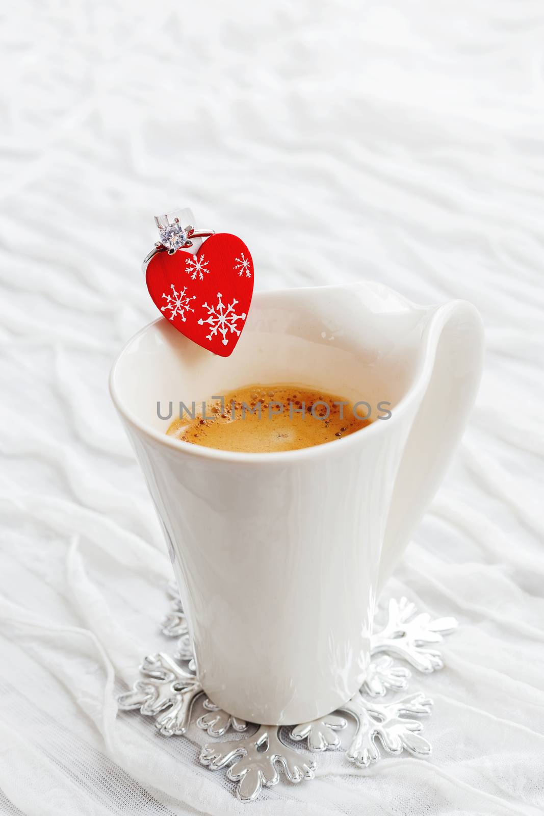 White cup of hot coffee with decorative heart and engagement diamond ring, symbol of love and marriage. Valentine's day background with place for text.