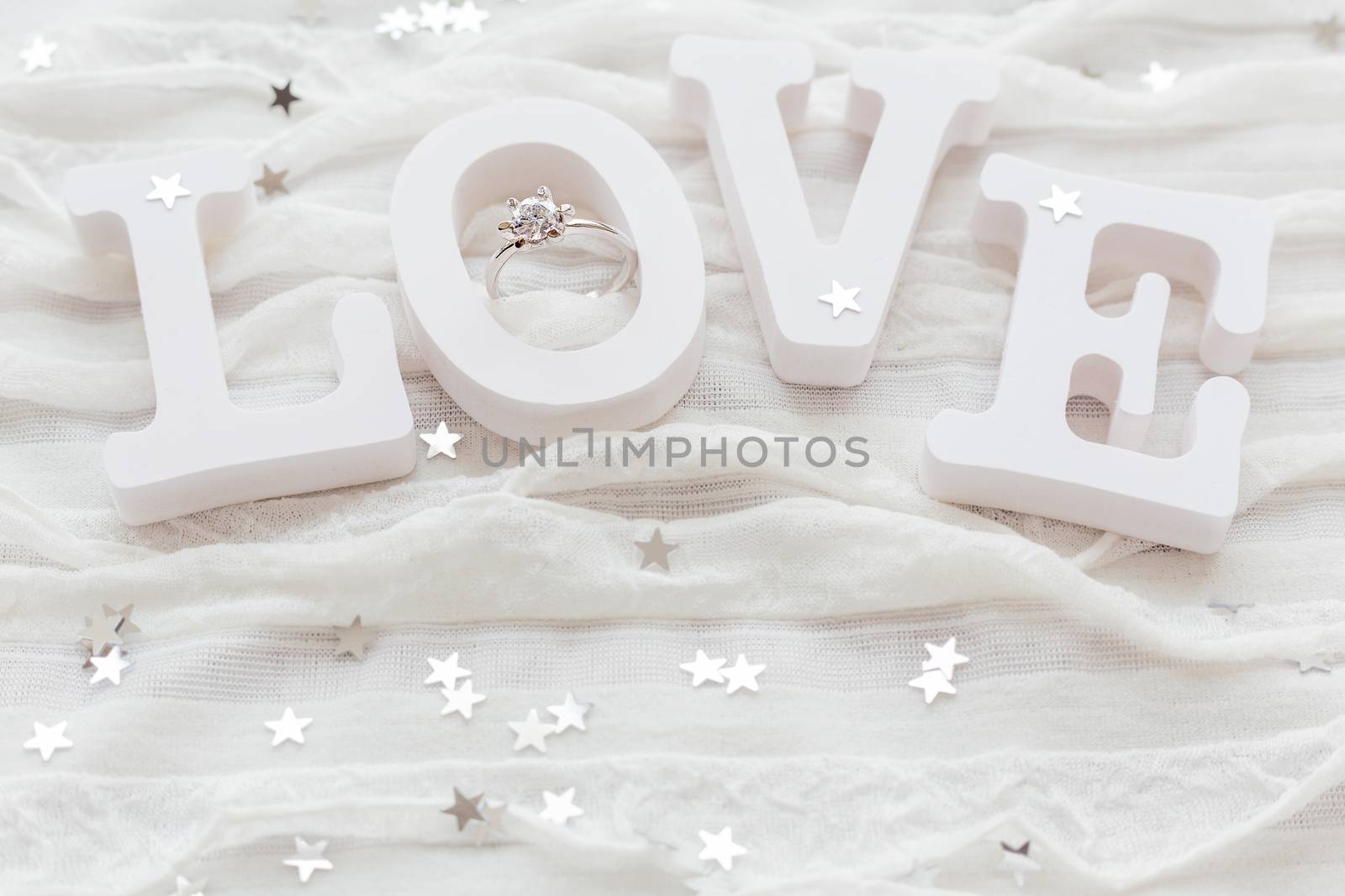 Word LOVE on white fabric background with engagement diamond ring. Good for Valentine's day cards. Place for text.