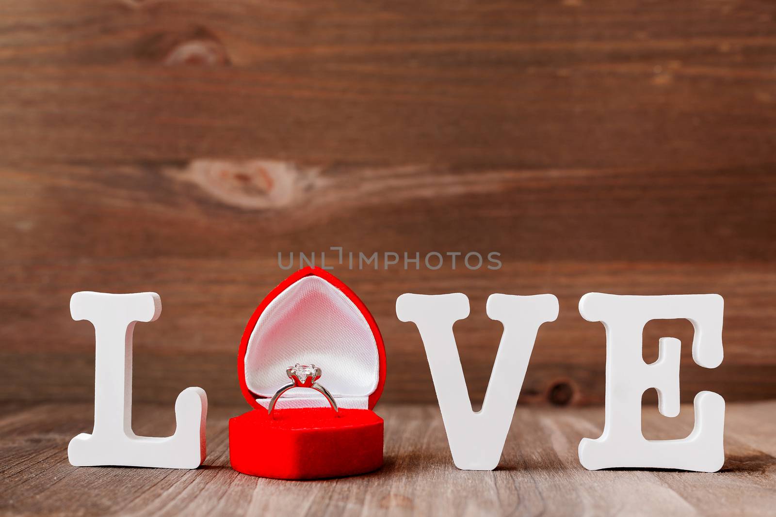 Word LOVE and diamond engagement ring in red gift box on wooden background. Symbol of love and marriage. Good as Valentine's Day card with place for text.