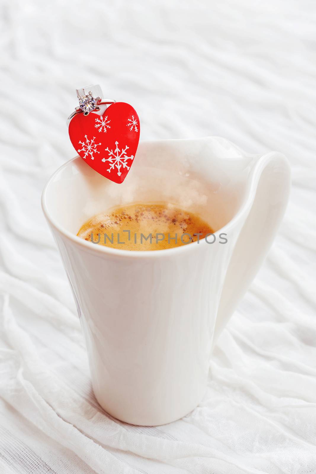 White cup of hot coffee with decorative heart and engagement diamond ring, symbol of love and marriage. Valentine's day background with place for text.