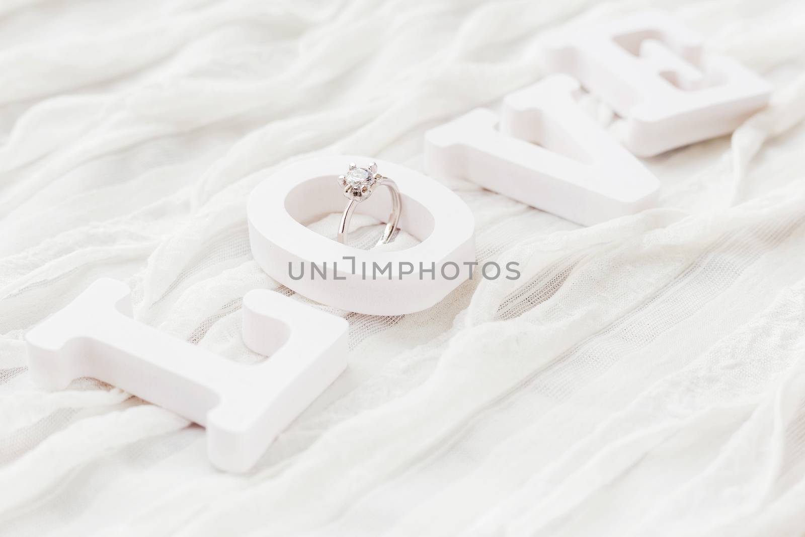 Word LOVE on white fabric background with engagement diamond ring. Good for Valentine's day cards.