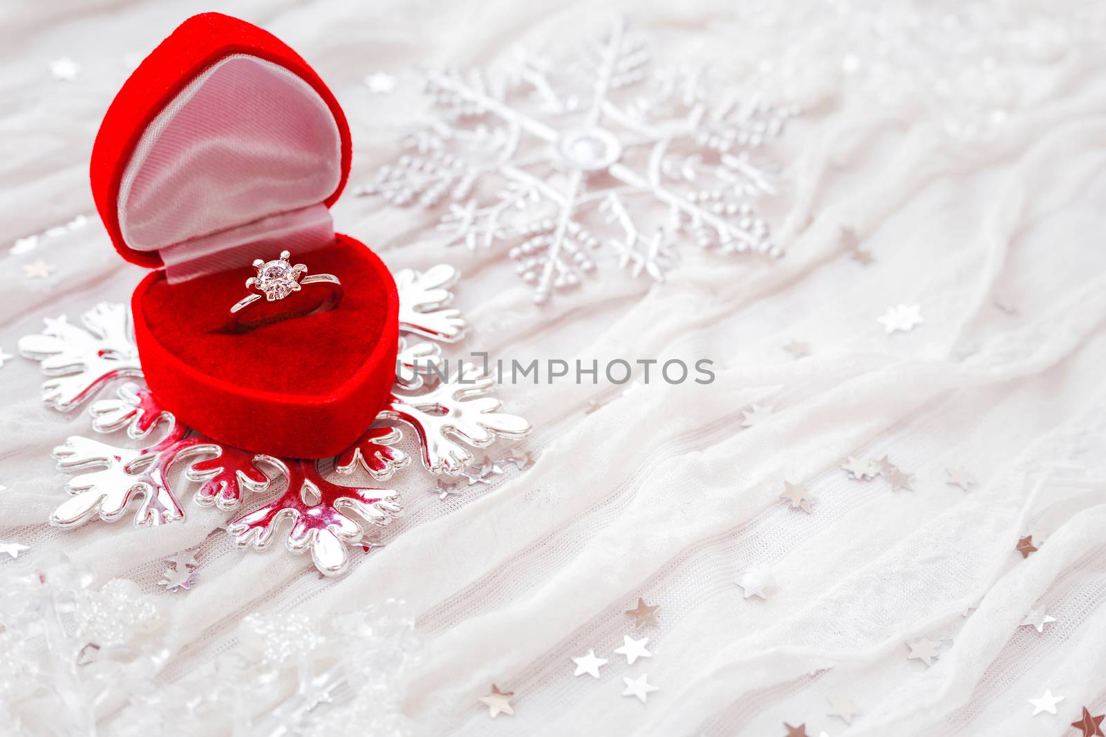 Engagement diamond ring in red gift box on white fabric background. Good for Valentine's day cards. Place for text.