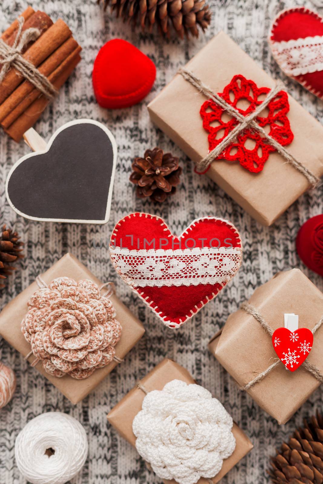 Valentine's Day symbols - hearts, presents in craft paper with crochet flowers, pine cones, red jewelry gift box - on knitted background.