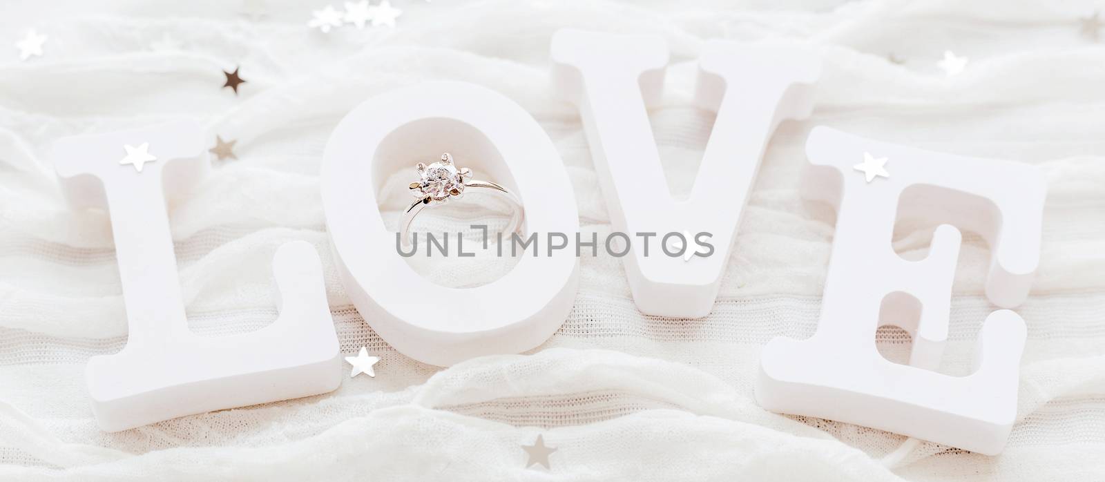 Word LOVE on white fabric background with engagement diamond ring. Good for Valentine's day cards. Place for text.