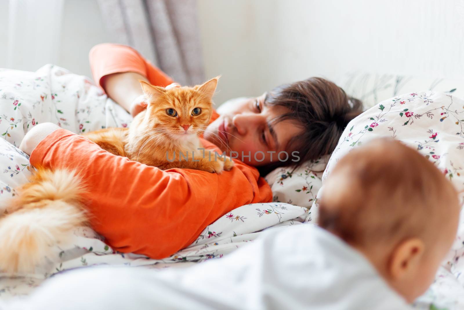 Man with baby and ginger cat in bed. Cute cozy home background. Morning bedtime. Smiling father with little son.