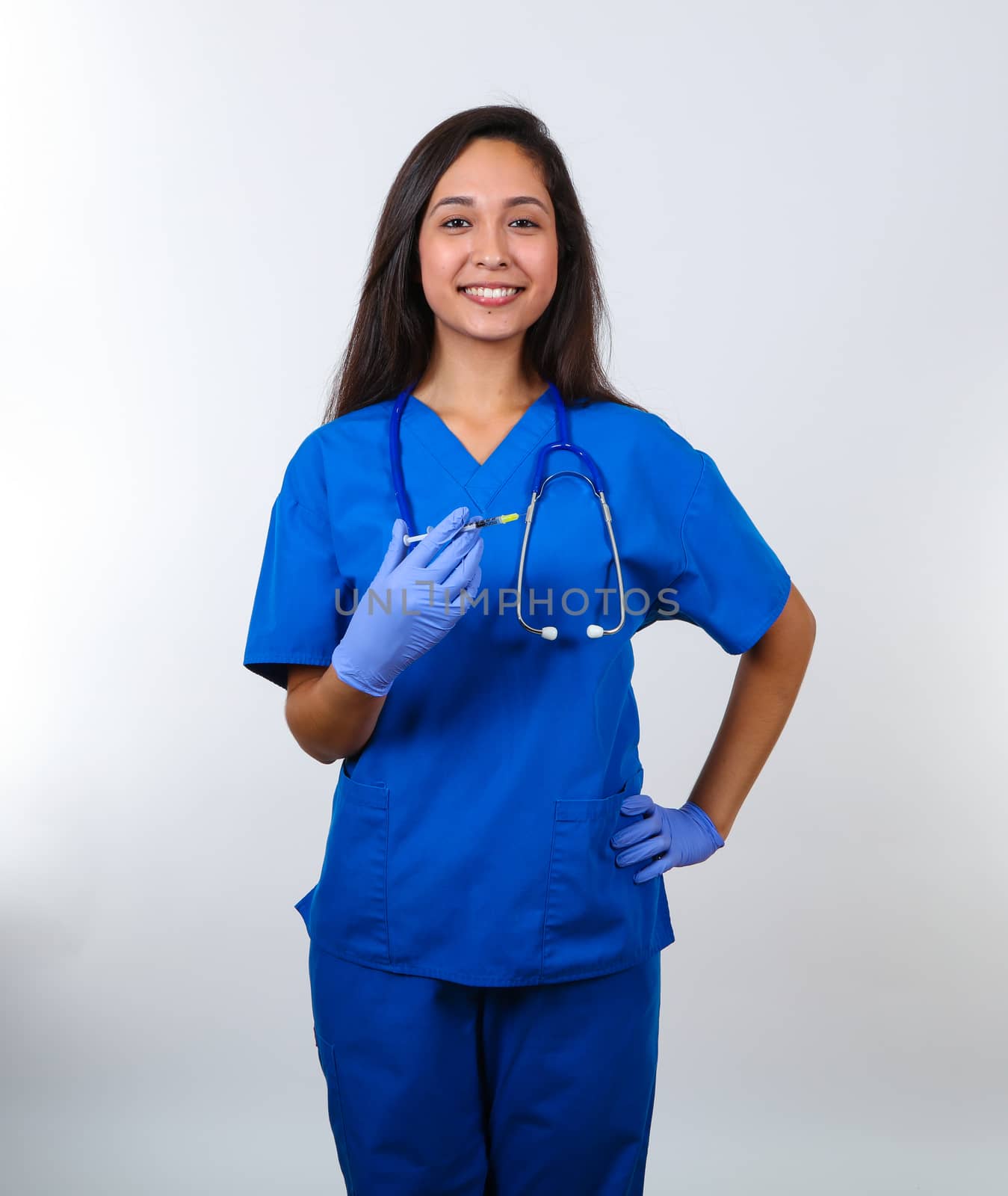 An attractive nurse in blue scrubs proudly holds a vaccine.