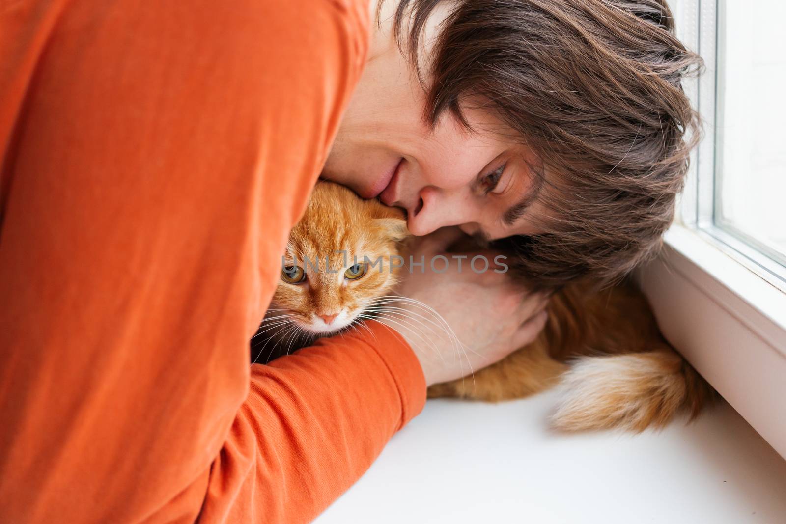 Man in orange sweatshirt is hugging cute ginger cat. Pet adoption. Ex-stray cat at home. Fluffy pet and it's master.