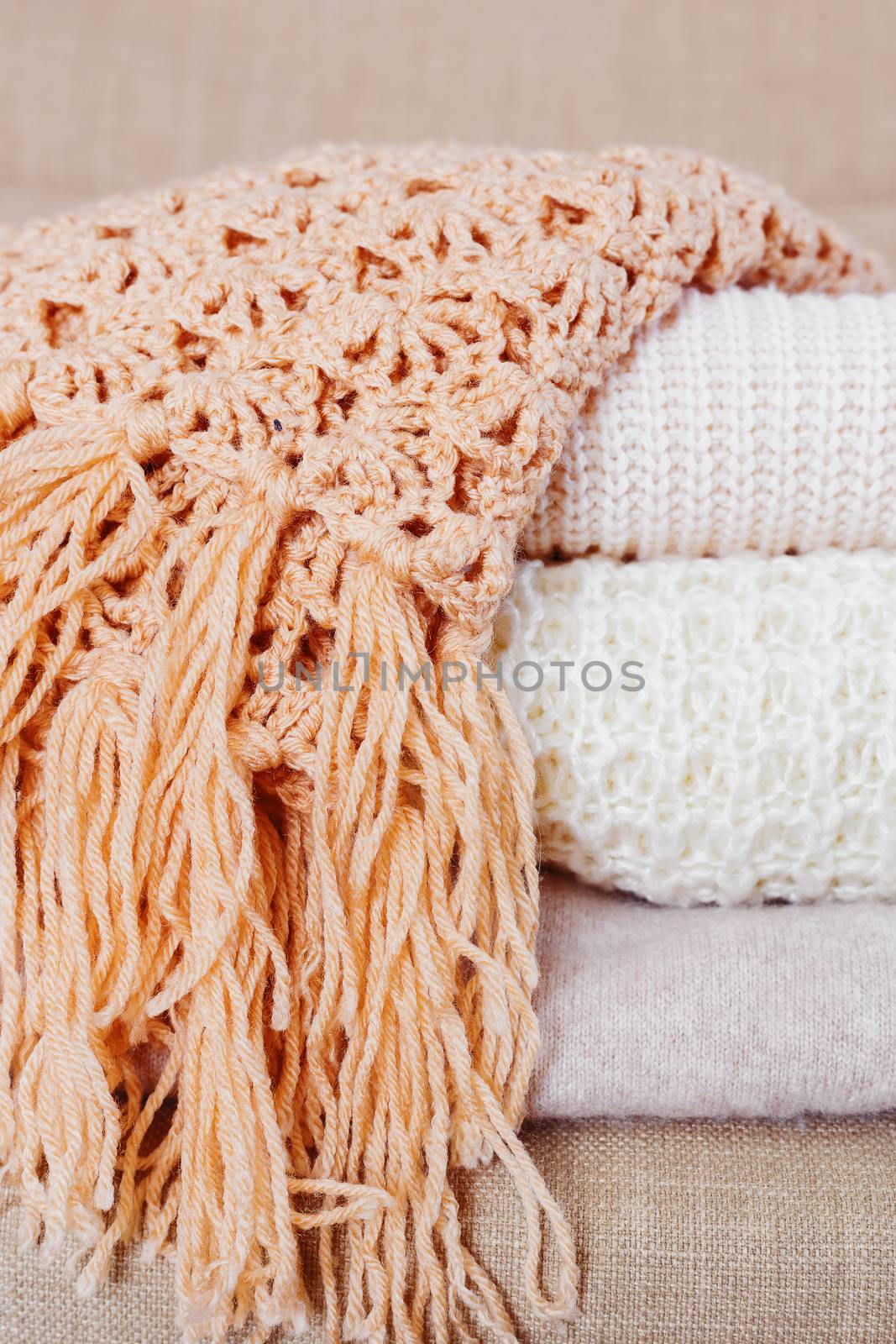 Pile of beige woolen clothes. Warm knitted sweaters and scarfs are folded in one heap.