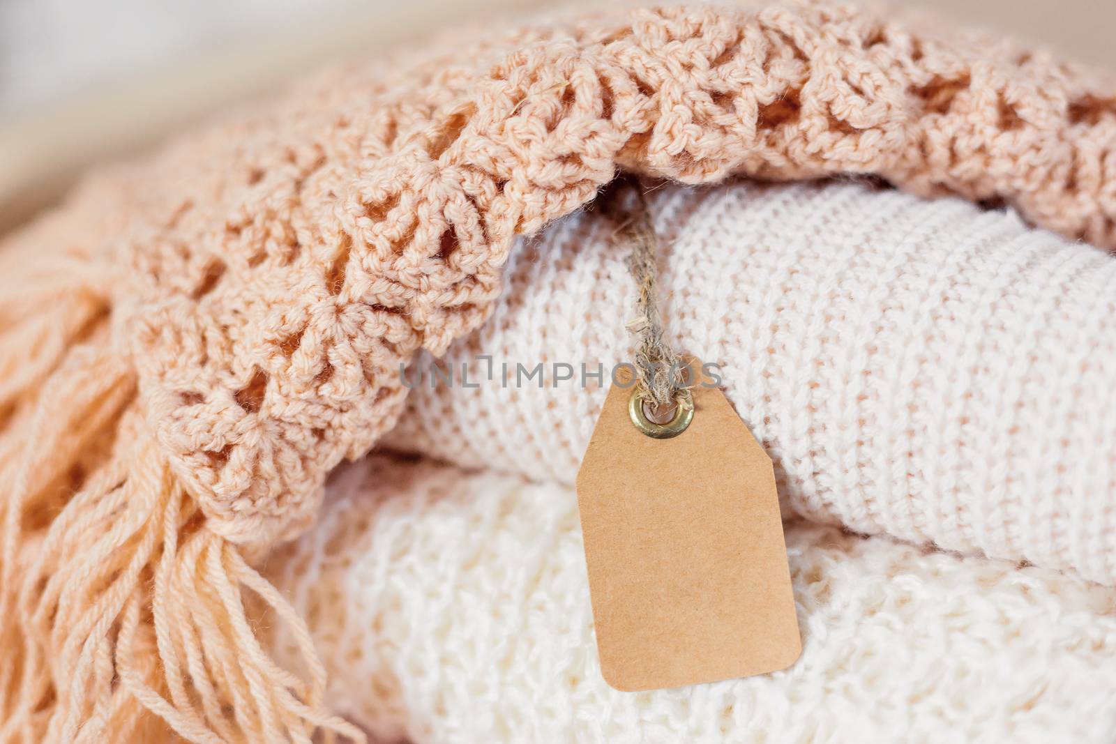 Pile of beige knitted clothes. Crochet warm scarfs and sweaters are folded in one heap. Place for text on clear tag.